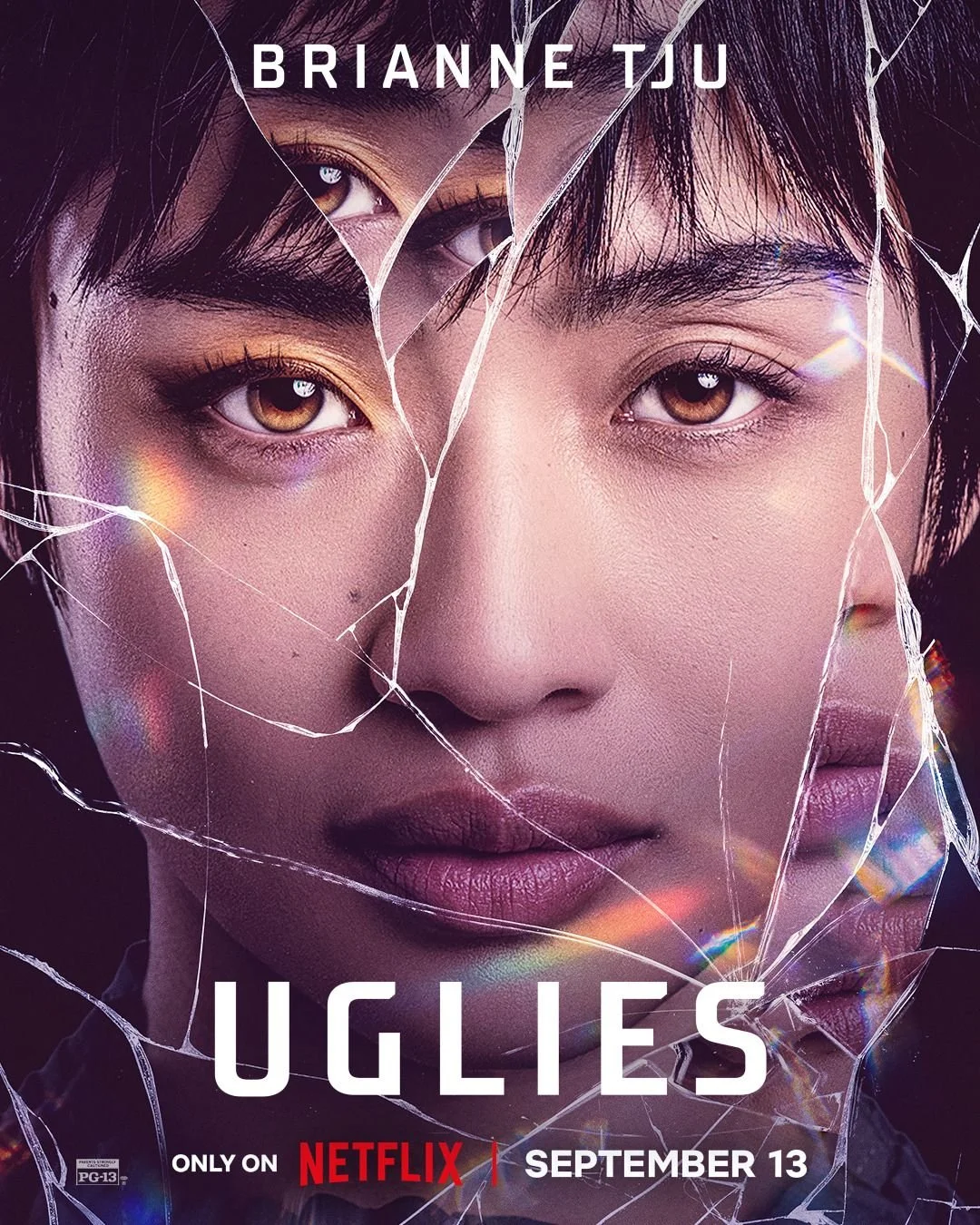 Close-up of a woman's face with cracked glass over it, promotional poster for the Netflix film 'Uglies' starring Brianne Tju, releasing September 13.