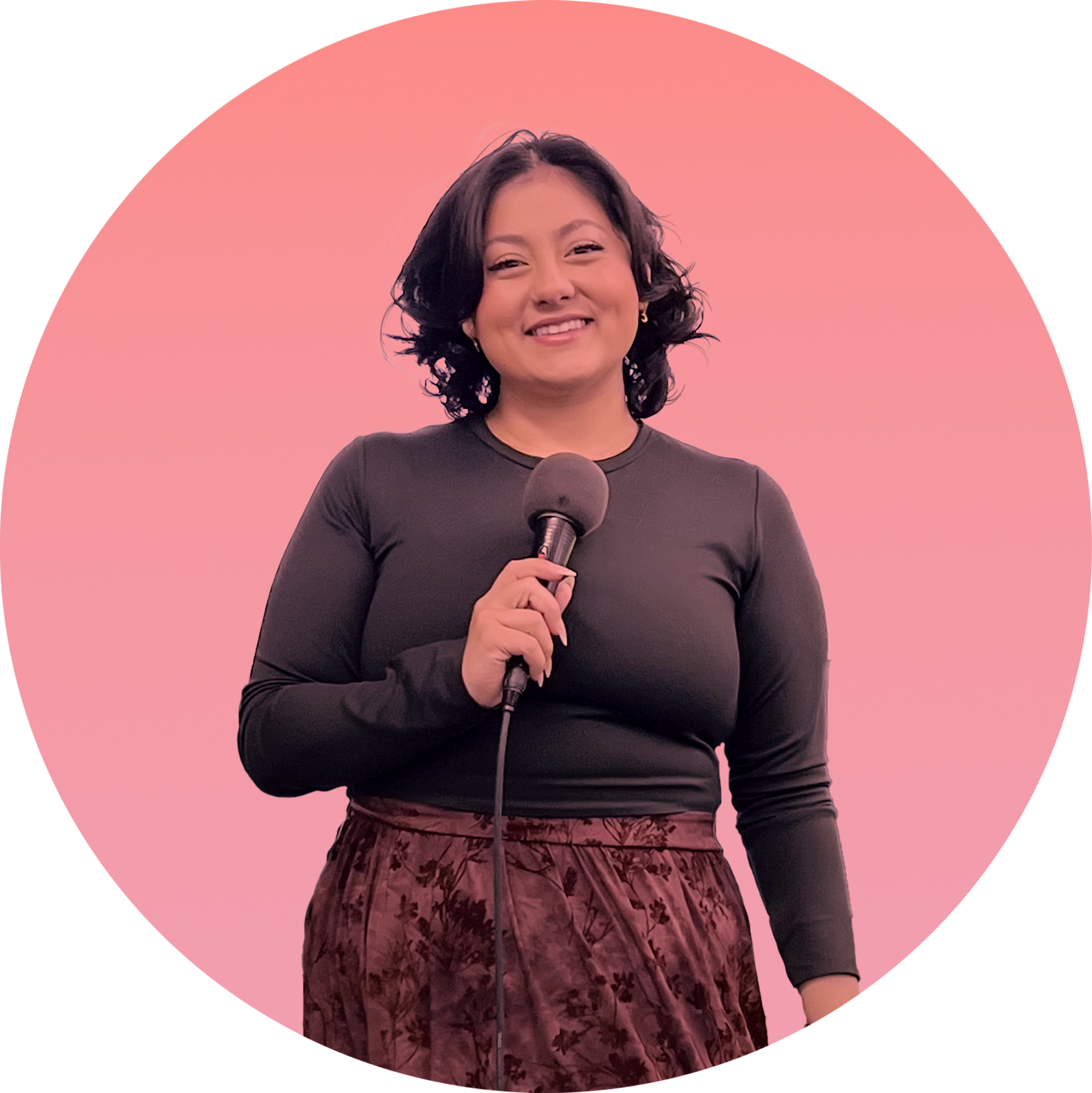 Woman with wavy black hair smiling, holding a microphone against a pink background.