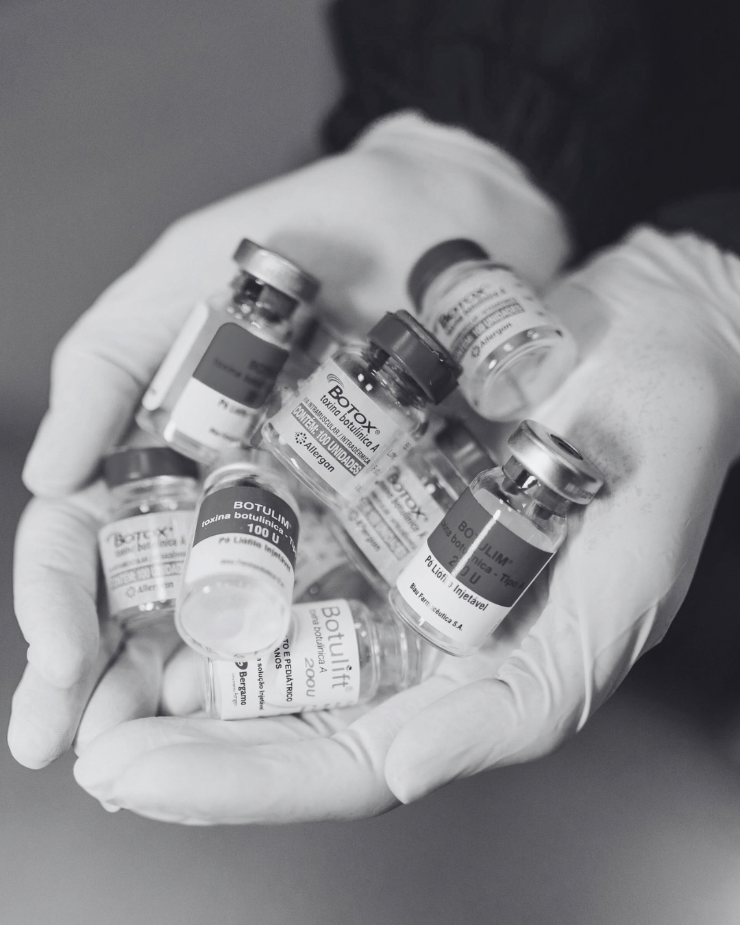 A person's hand wearing a latex glove holding several small glass vials labeled with medical information.