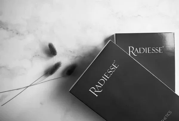 Two Radiesse skincare product boxes and a small sprig of dried flowers on a light-colored surface.