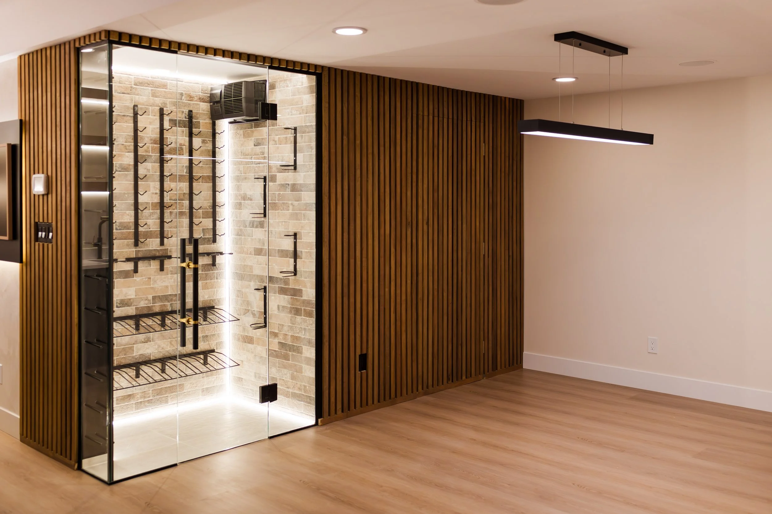Modern glass enclosed sauna with brick walls, black metal racks, and warm wood paneling, inside a spacious room with hardwood flooring and minimalistic lighting.