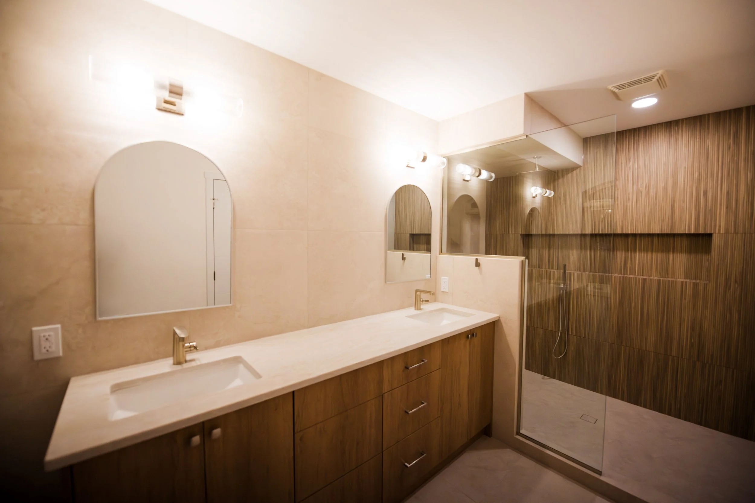 Modern bathroom with dual sinks, wooden cabinets, mirrors, and a walk-in shower with wooden wall tiles.