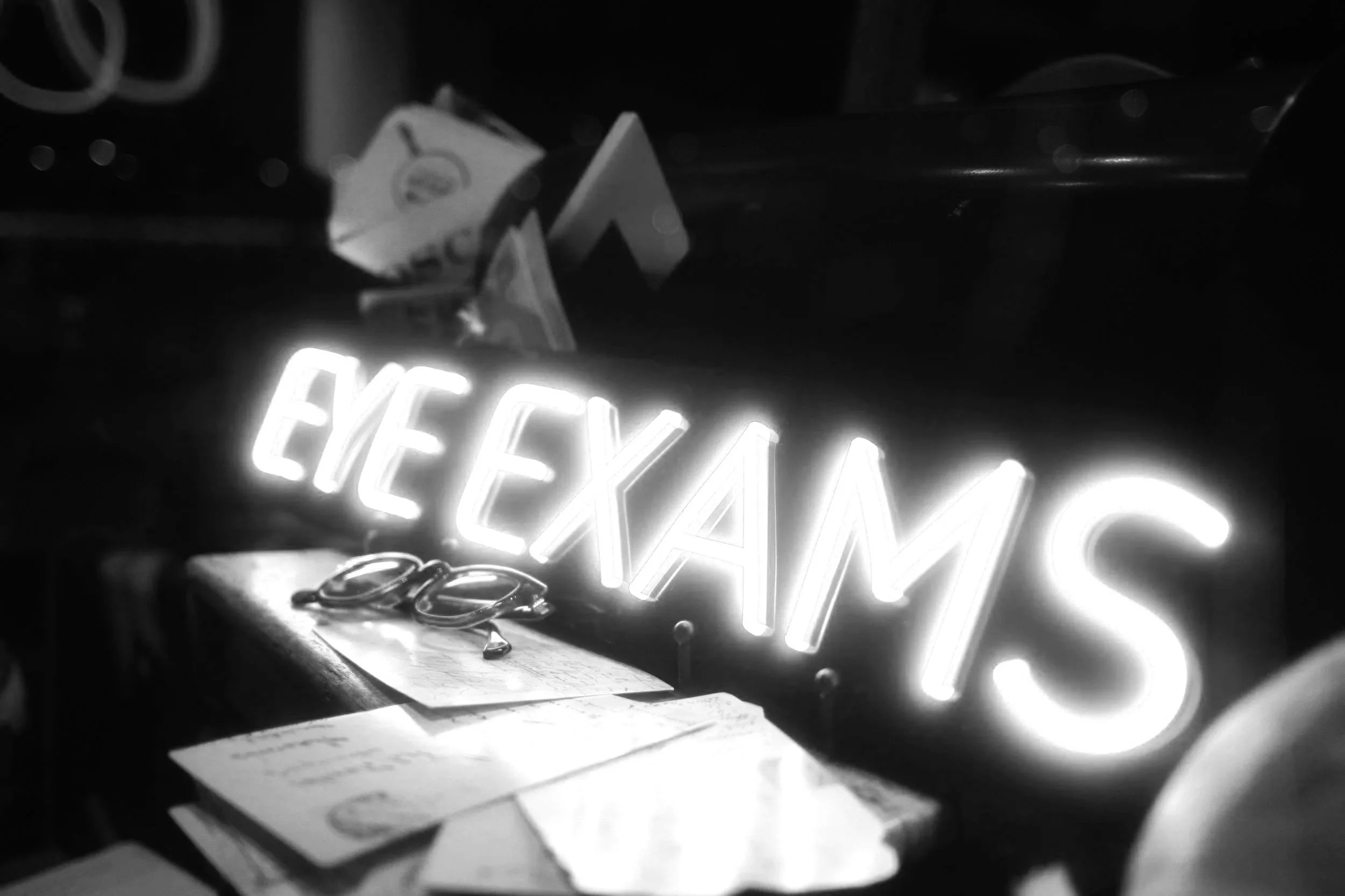 Black and white photo showing a neon sign reading 'EASY' and a partially visible pair of glasses.