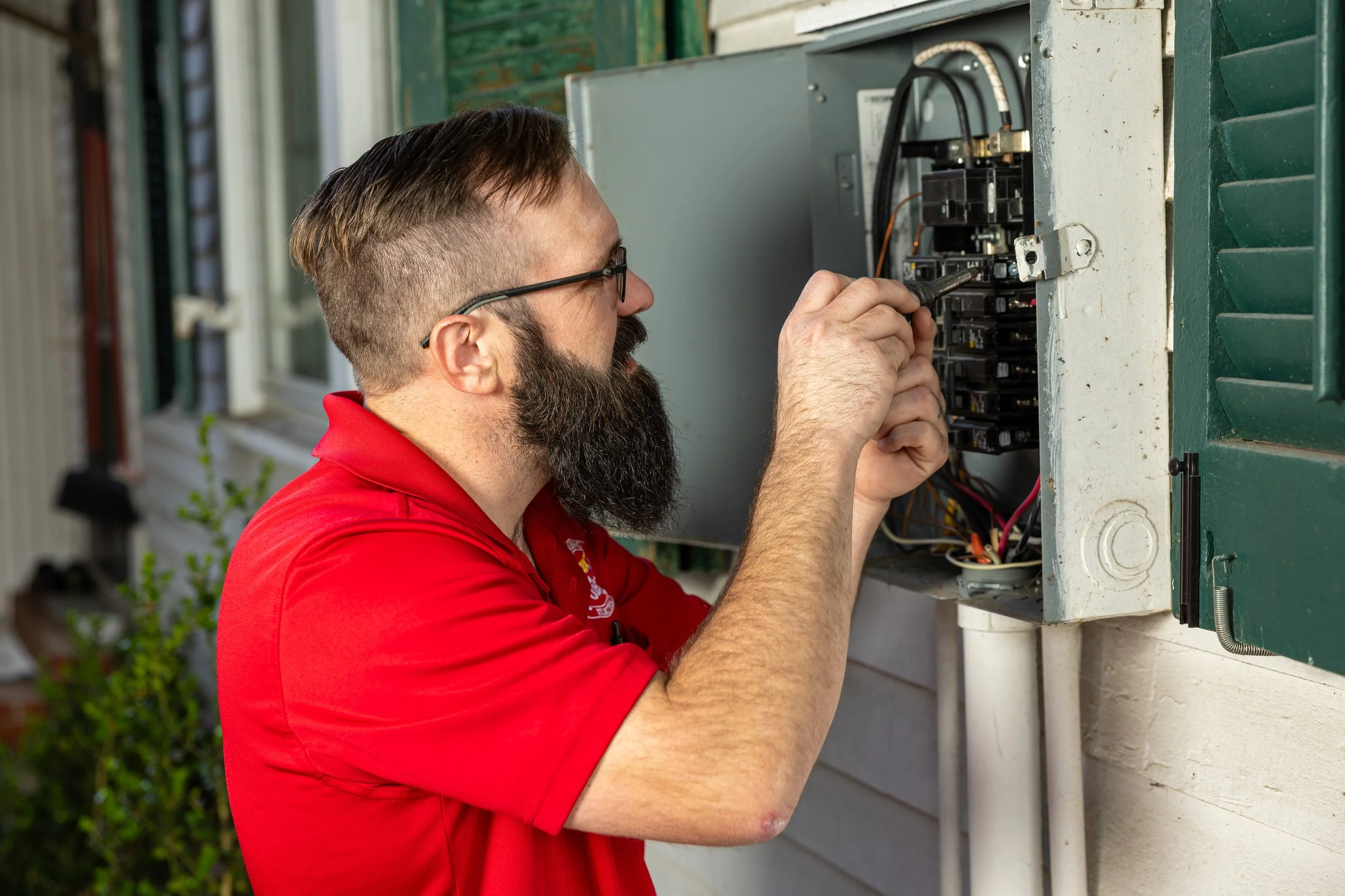 A man with glasses and a beard working on an outdoor electrical breaker panel.