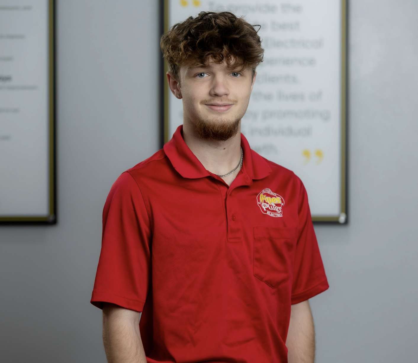 A young man with brown curly hair and a beard wearing a red polo shirt with a McDonald's logo standing indoors against blurred signage background.