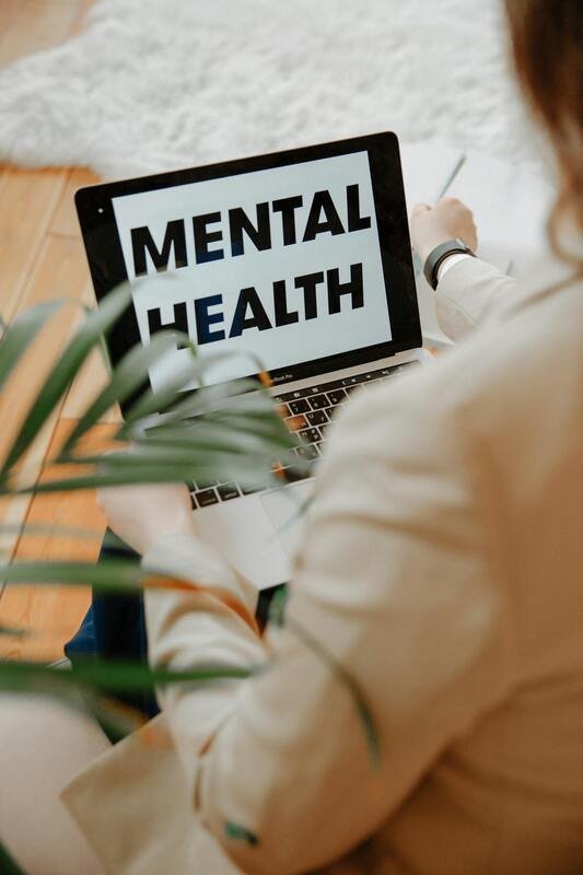 Person holding laptop with the words 'Mental Health' on the screen, with some plants partially visible in the foreground.