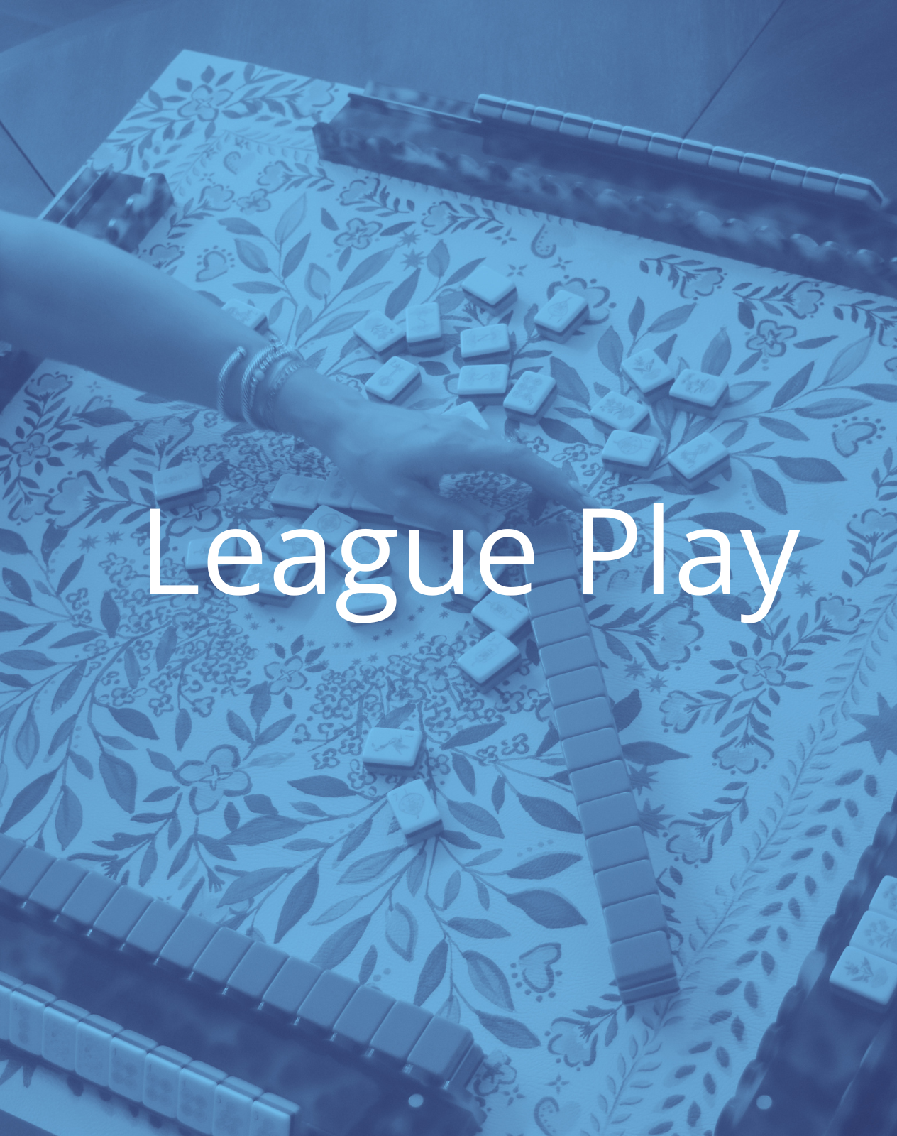 A person playing mahjong at a table with a floral tablecloth, with mahjong tiles scattered around and a mahjong set in the background, overlaid with the text 'League Play'.