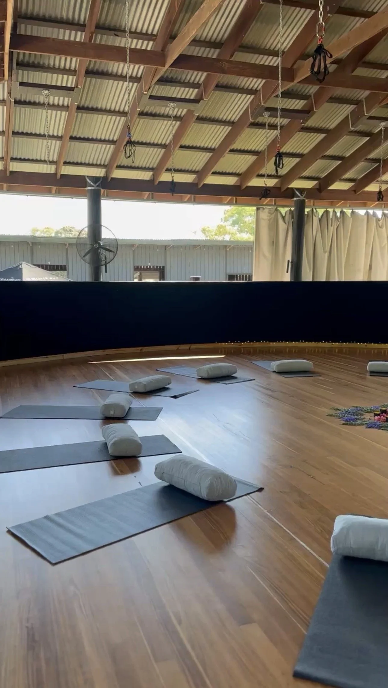 Modern wooden building with large glass window, set against mountainous landscape with dry grassy terrain in the foreground.