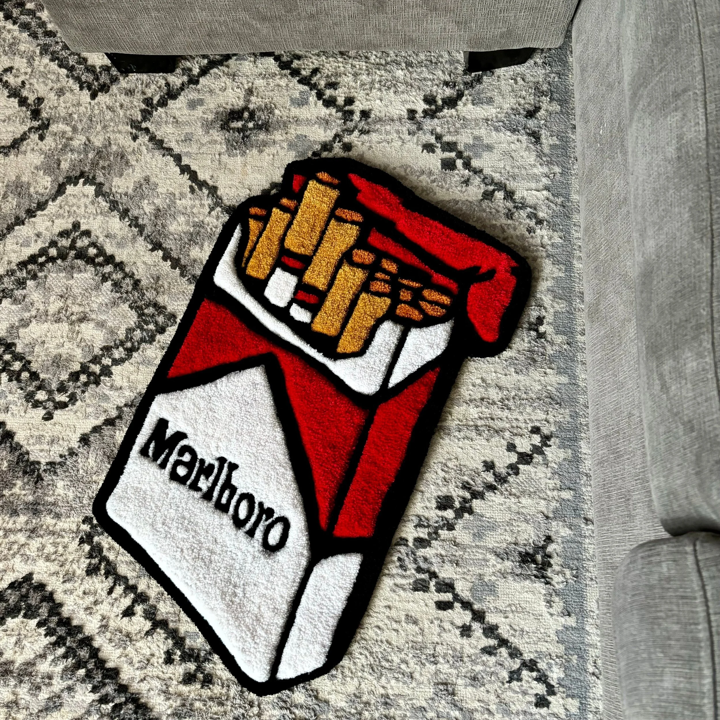 Colorful patch of French fries in a Red and white cardboard container with the word 'Enjoy' written on it, placed on a patterned rug.