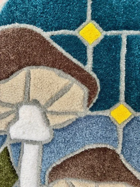 Close-up of a colorful decorative rug with mushrooms in brown and white, and blue and yellow geometric patterns.
