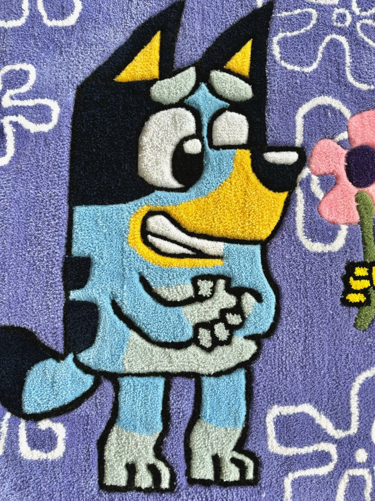 Colorful cartoon dog, with tears in its eyes, holding its hands together, standing on a purple background with white decorative swirl patterns, next to a pink flower with a black center and green stem.