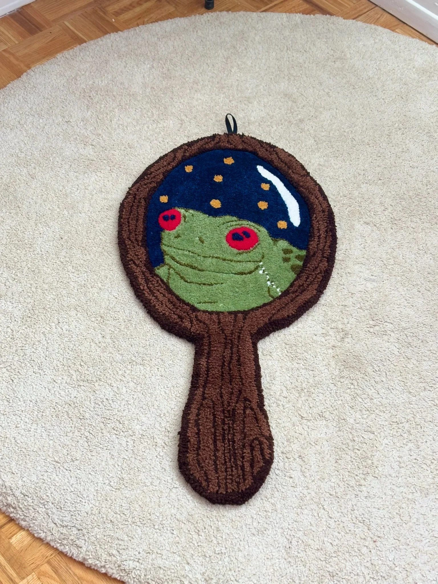 A circular rug with a tree trunk design and a mirror featuring a frog and starry night scene, placed on a wooden floor.