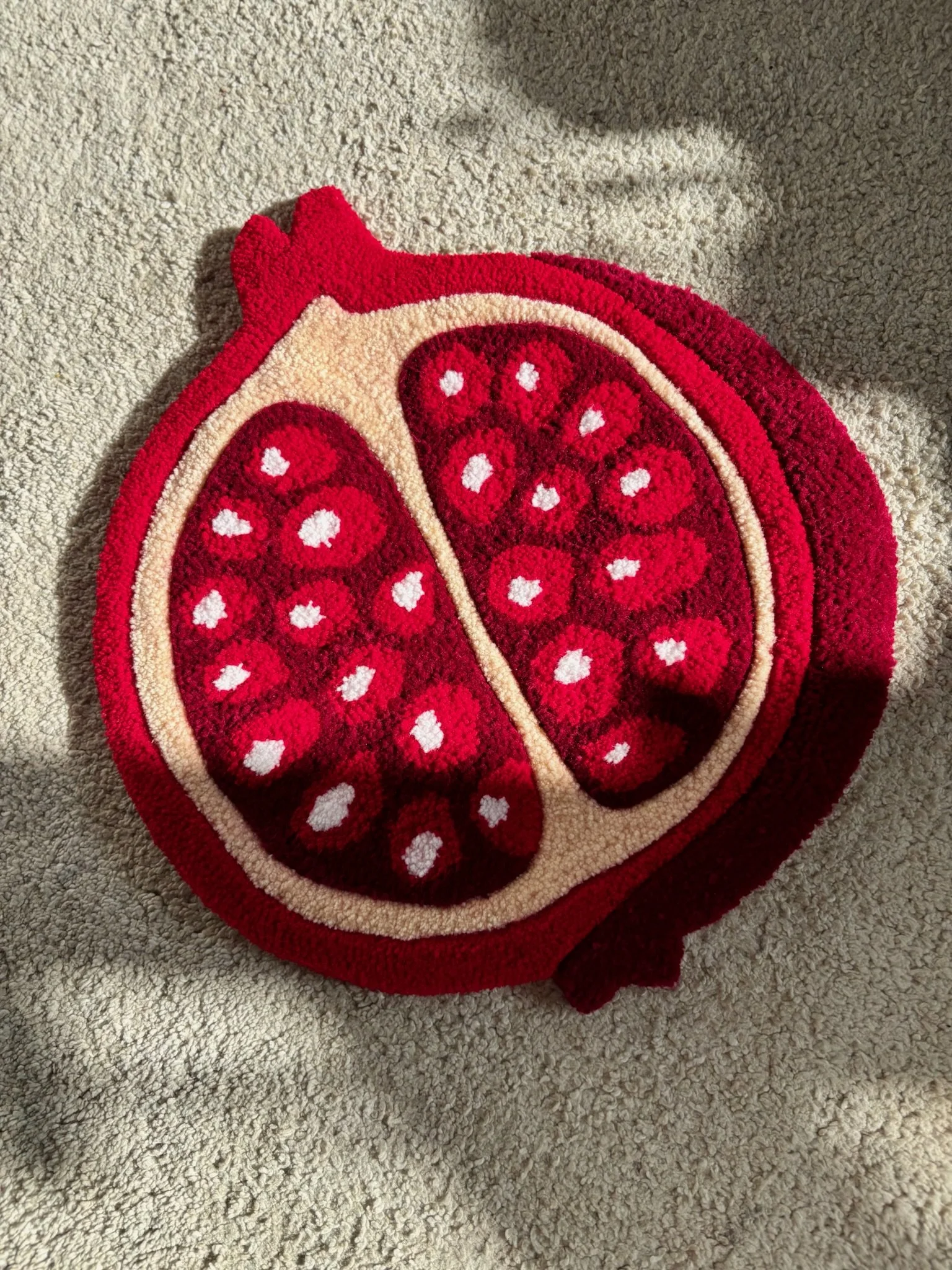 A colorful rug designed like a halved pomegranate fruit on a beige carpeted floor.
