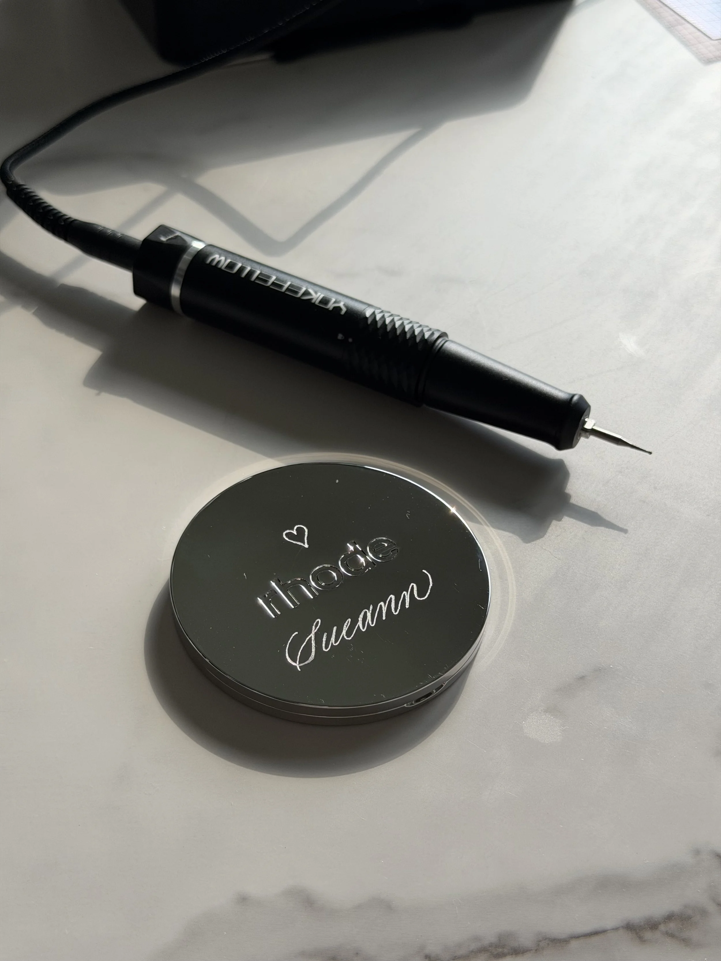 Rhode compact mirror personalized with custom hand engraving beside an engraving tool.