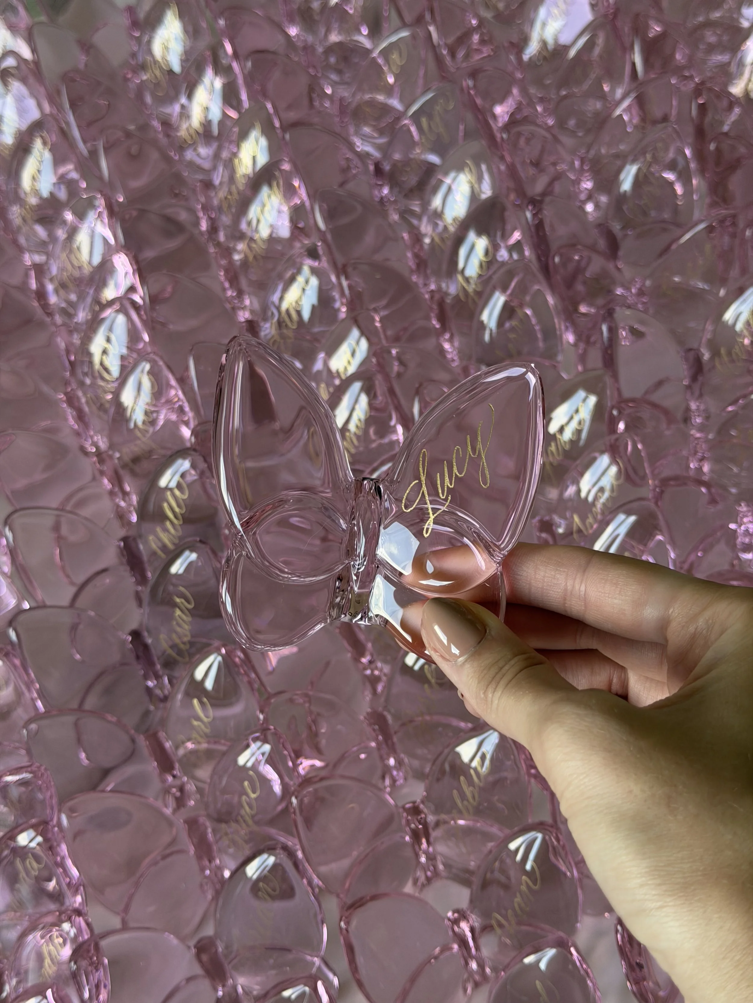Pink glass butterfly place cards personalized with guest names in gold calligraphy.
