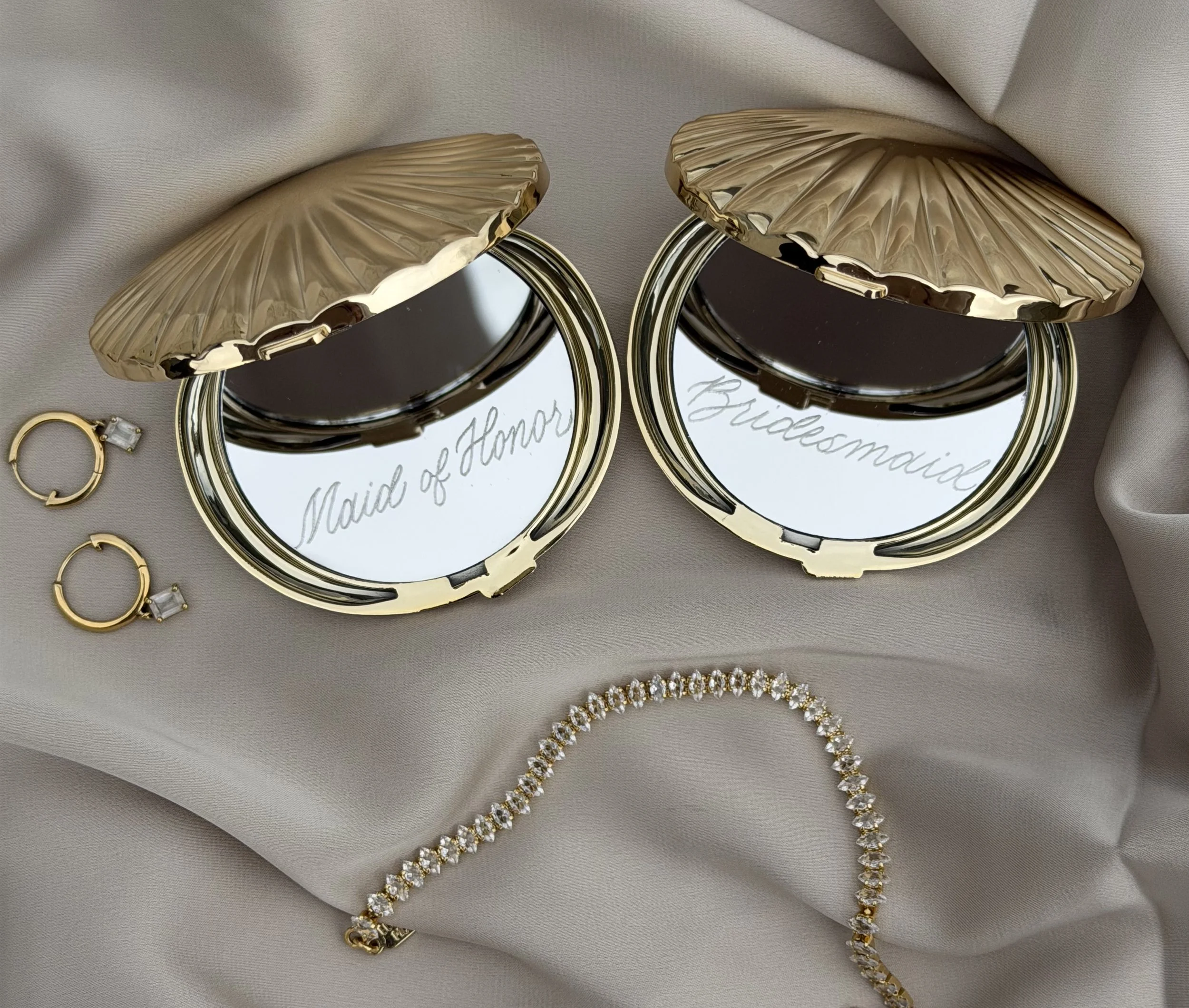 Seashell compact mirrors personalized with custom gold calligraphy, styled with jewelry.