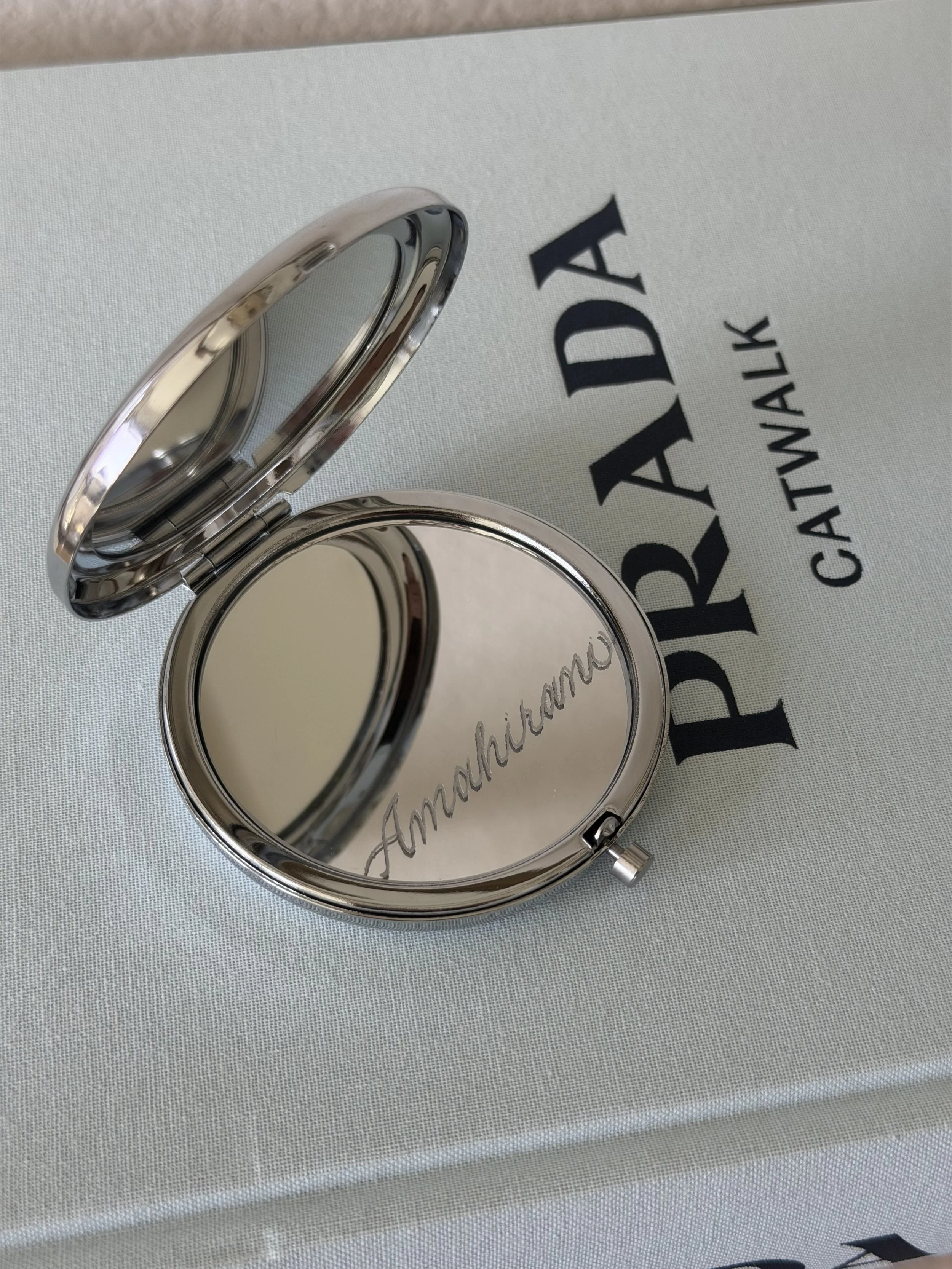 Compact mirror personalized with custom hand engraving, styled with a Prada book.