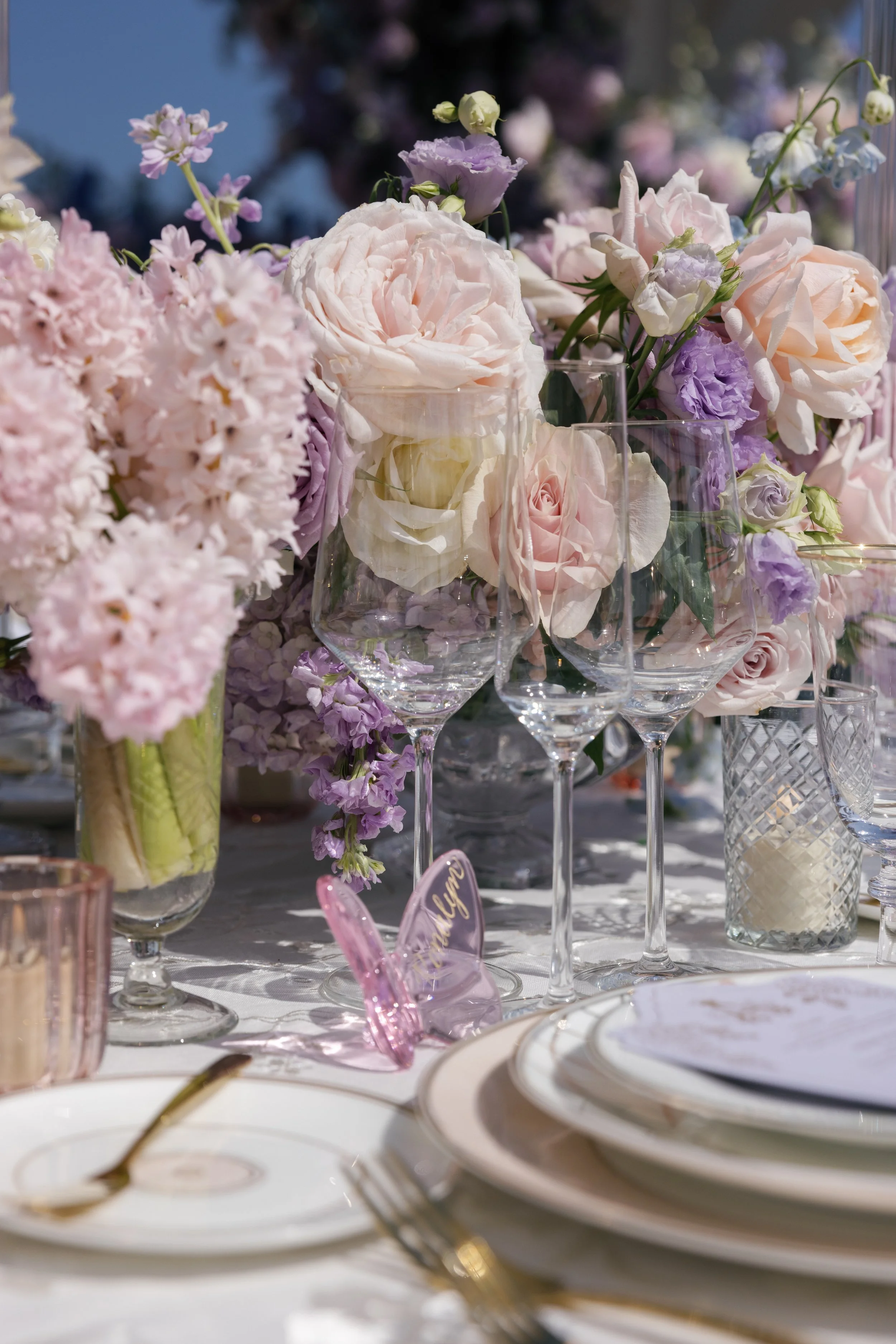 Pink glass butterfly place cards personalized with guest names in gold calligraphy at an elegant wedding table setting.