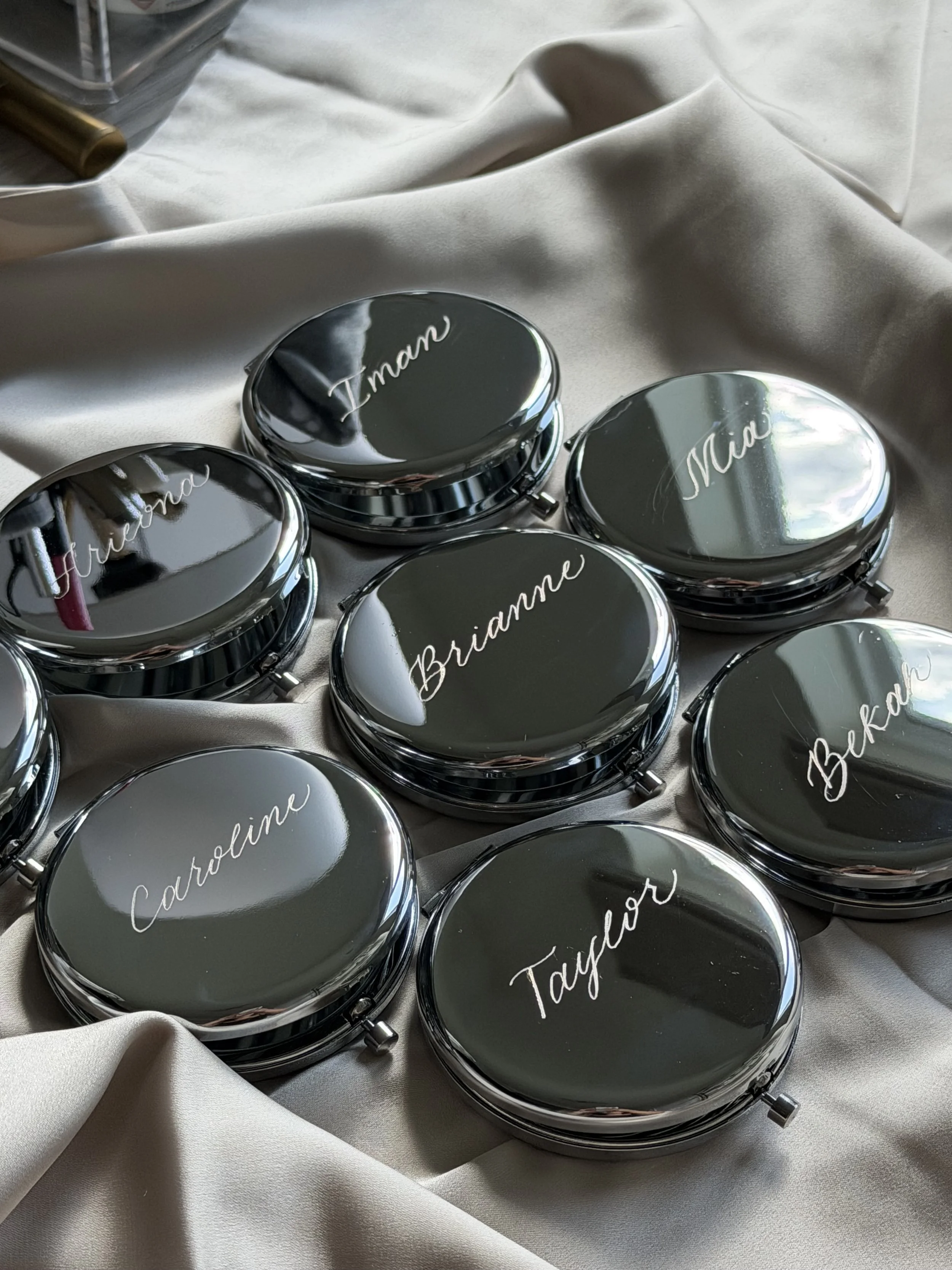 Personalized round compact mirrors engraved with individual names in custom calligraphy.