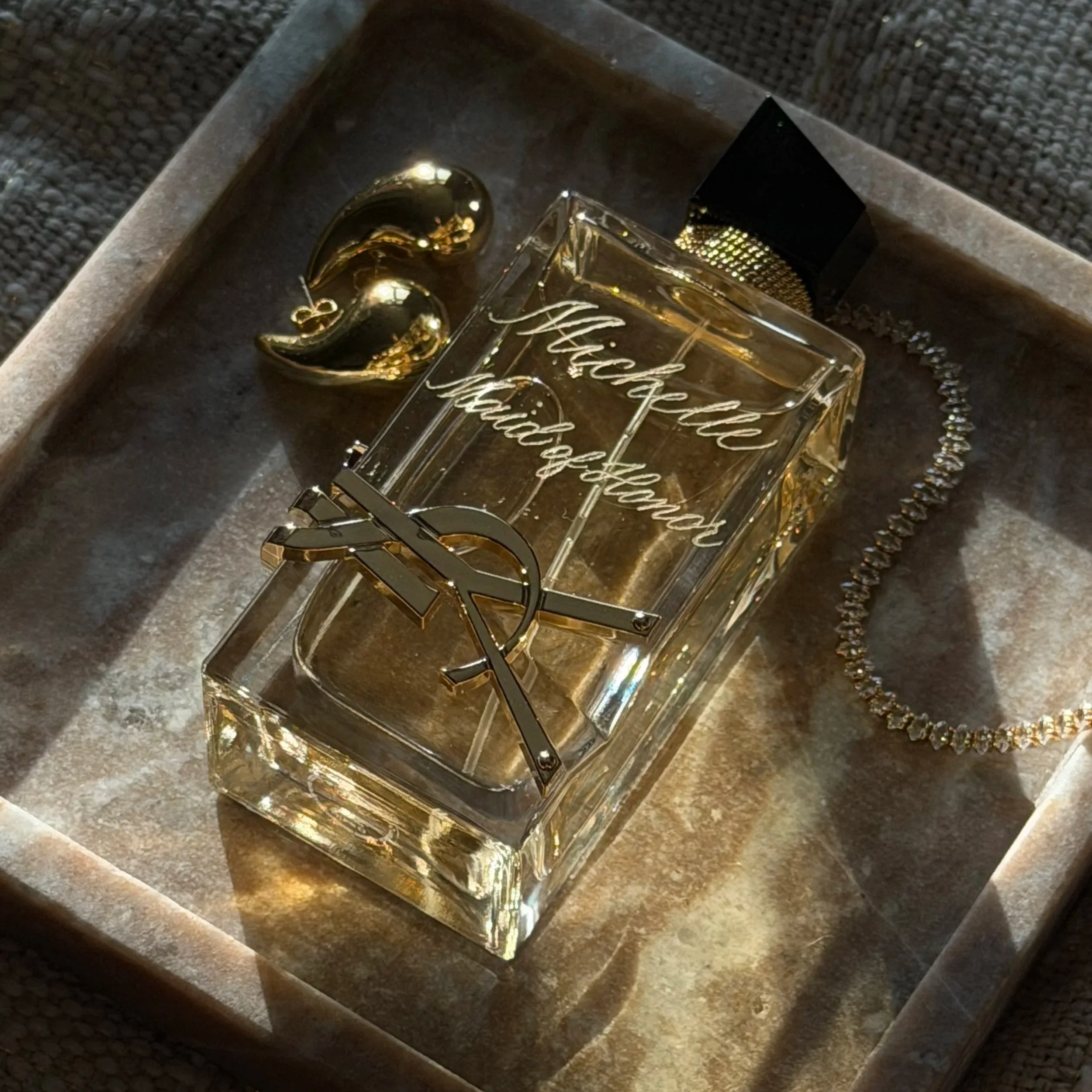 Hand engraved Yves Saint Laurent fragrance bottle with custom calligraphy, photographed with gold jewelry.
