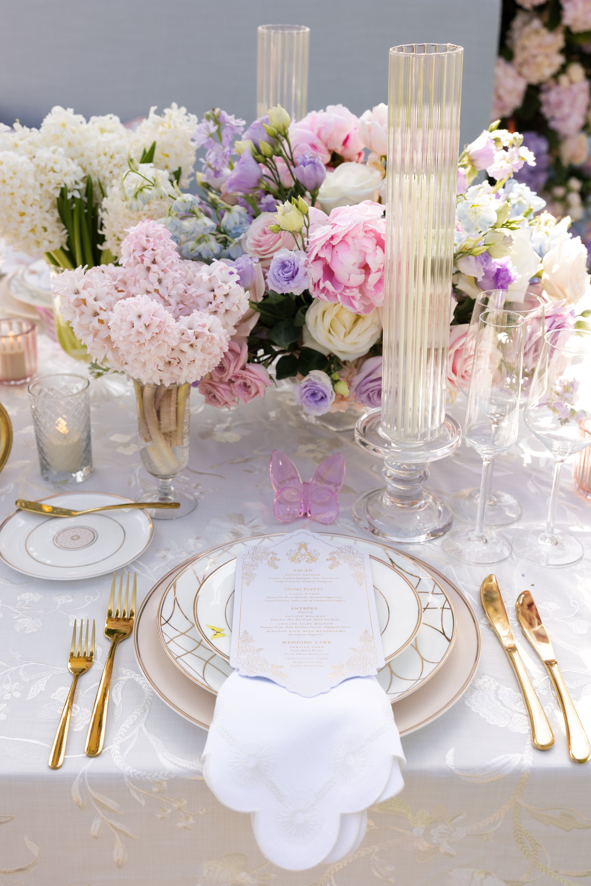 Pink glass butterfly place cards personalized with guest names in gold calligraphy at an elegant wedding table setting.