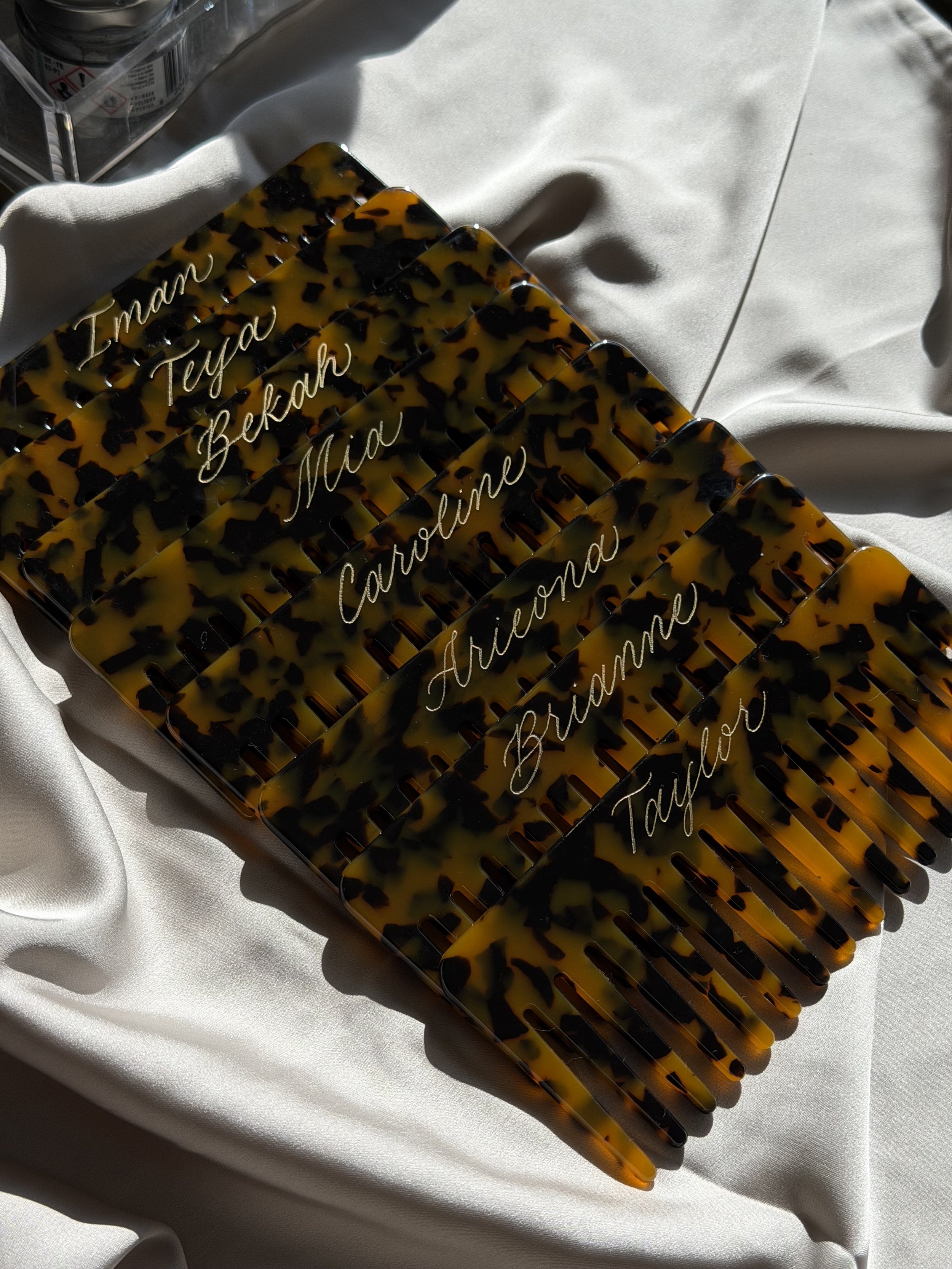 Personalized tortoise claw clips with names in gold calligraphy, styled on white satin.