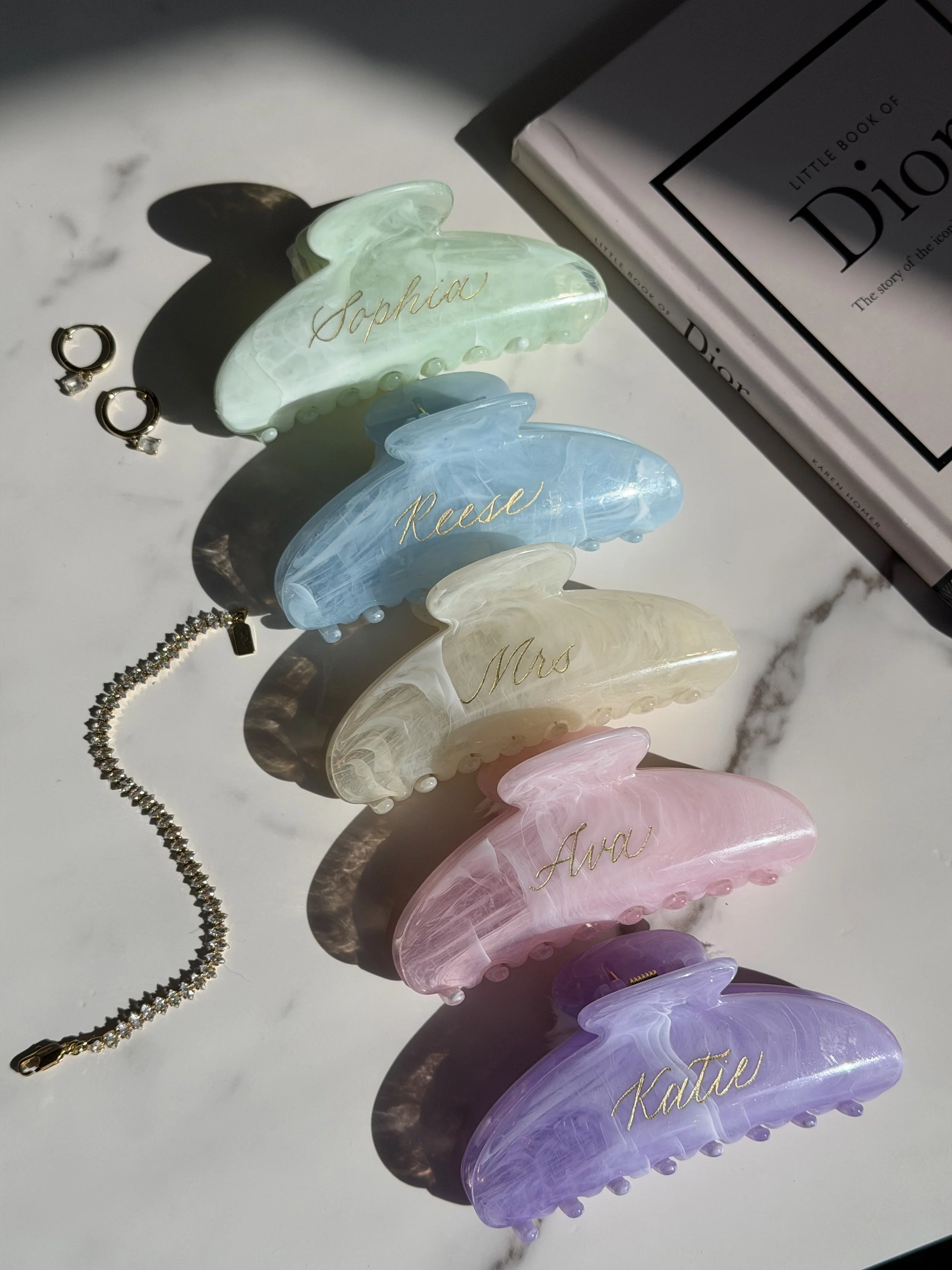 Colorful claw clips personalized with individual names in gold calligraphy.