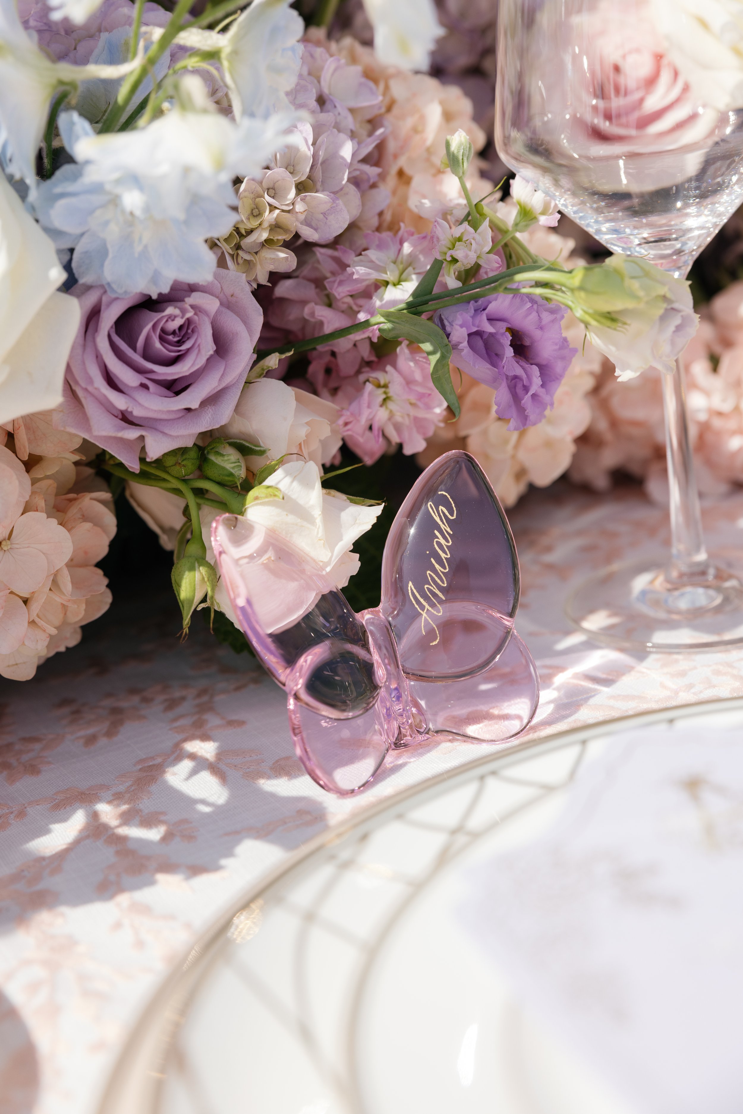 Pink glass butterfly place card personalized in gold calligraphy, styled with wedding florals.