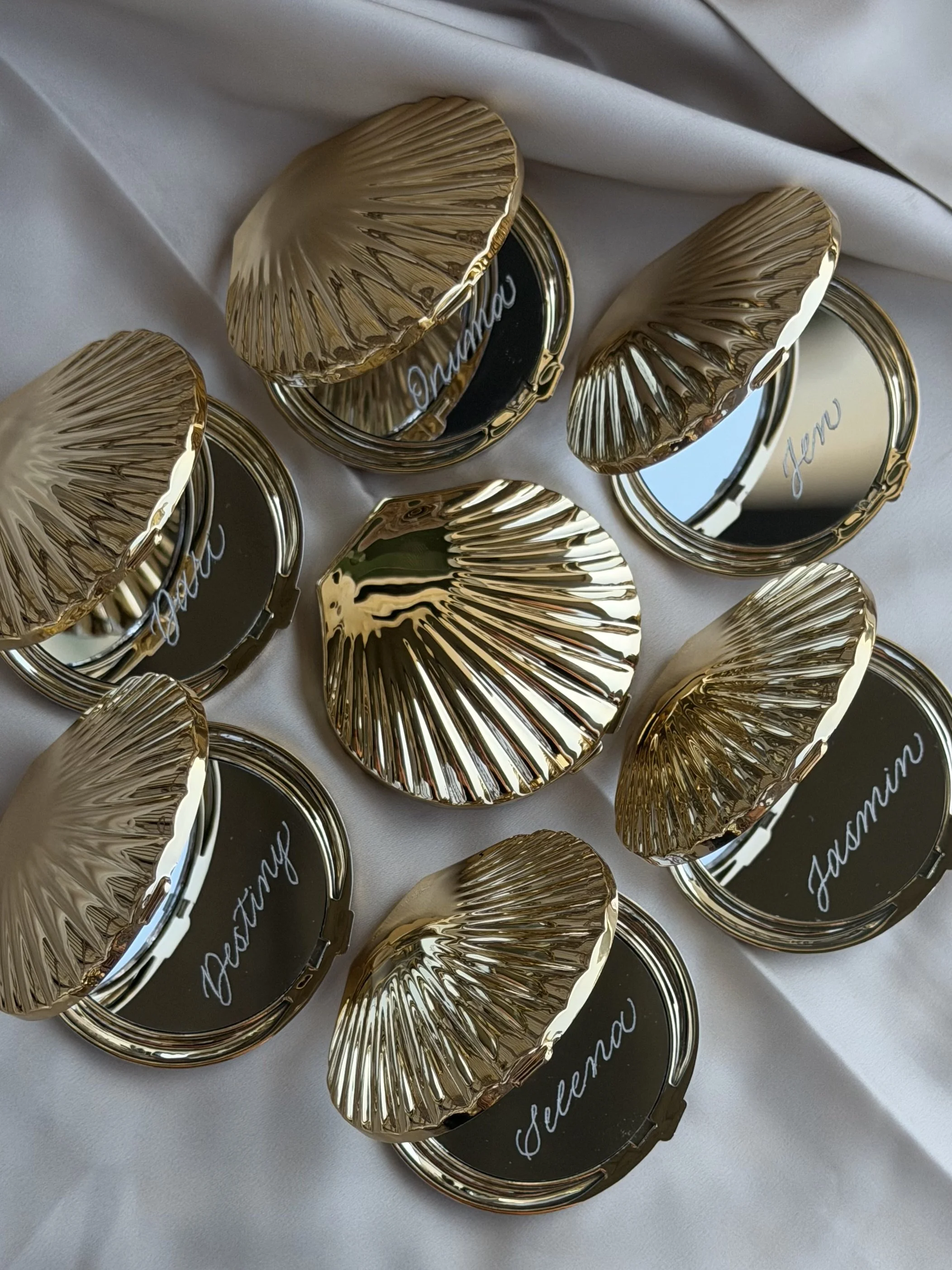Seashell compact mirrors personalized with individual names in custom calligraphy.