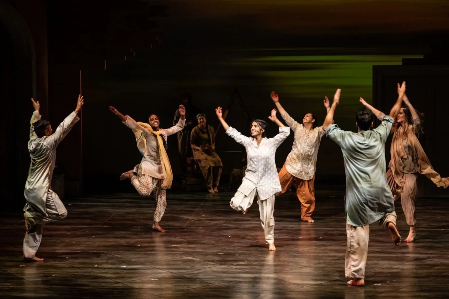 Group of performers dancing on stage, dressed in traditional Indian attire, with smiles and energetic poses.