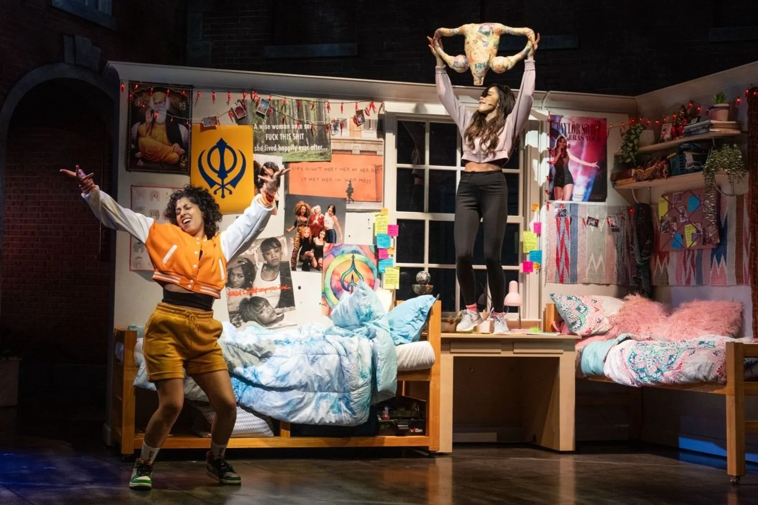 Two young women dancing and celebrating in a colorful bedroom with posters, photos, and decorations on the walls.