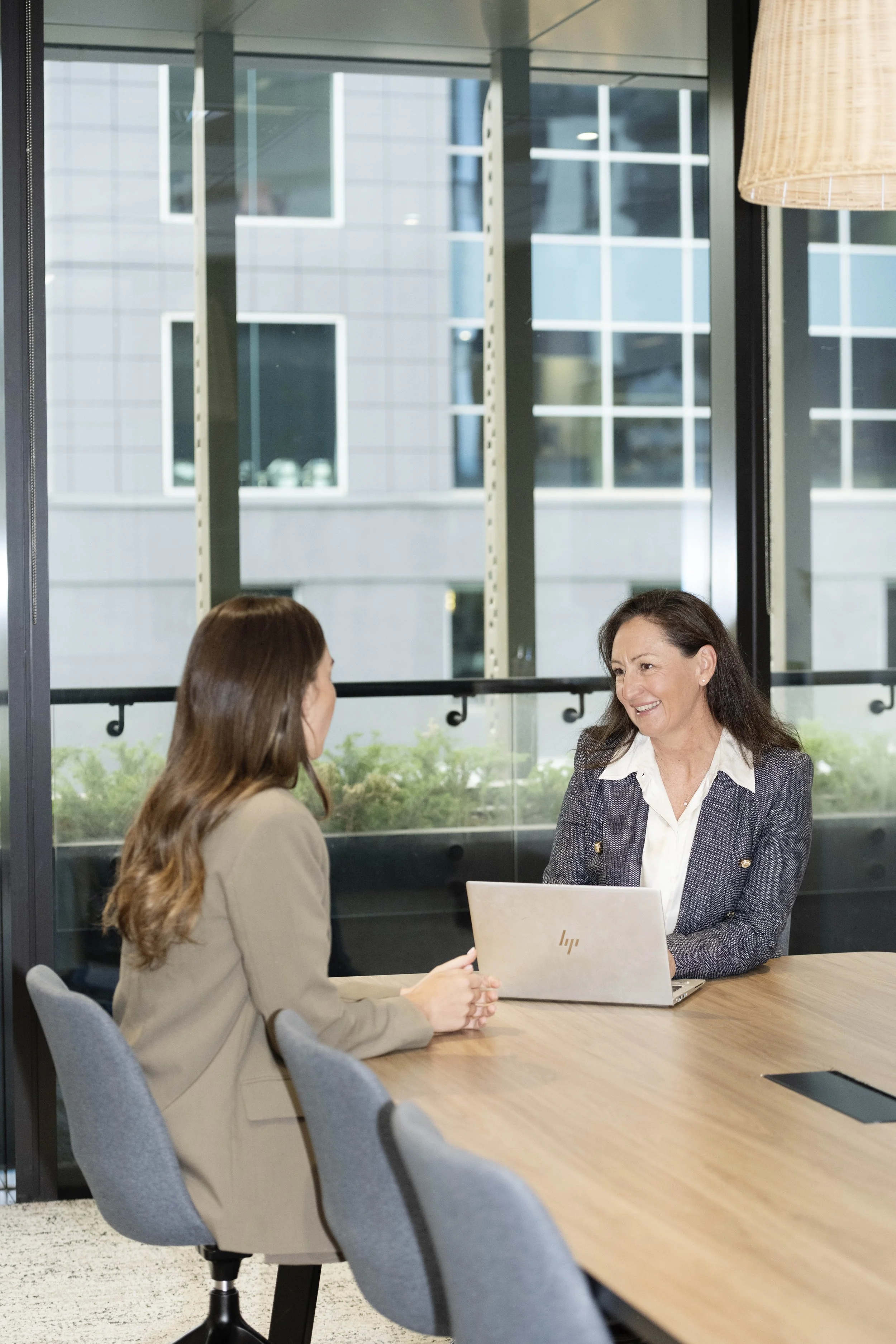 Sarah Pihan from SP Talent Solutions engaging in an interview, sitting at a conference table in a modern office with large windows. One woman has long brown hair, wearing a beige blazer, the other has shoulder-length brown hair wearing a grey blazer.