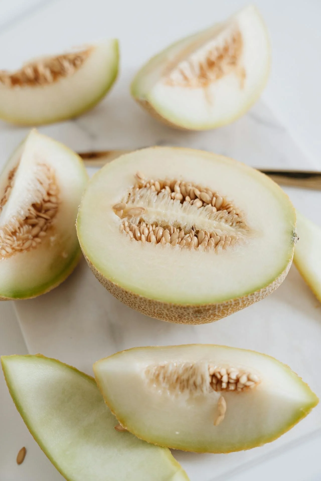 Sliced cantaloupe melon on a white surface with some pieces showing seeds and flesh.