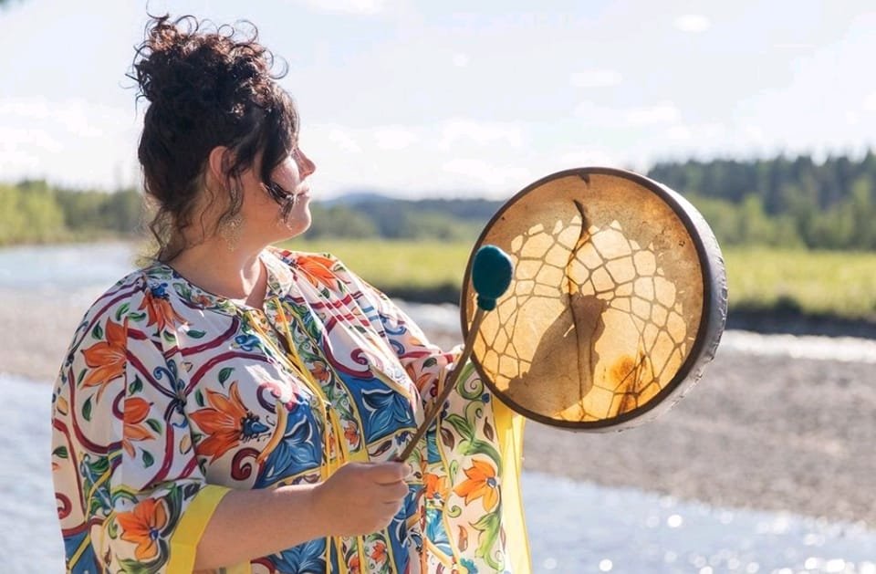 Woman holding a framed painting of a cat's face on a circular canvas outdoors on a sunny day.
