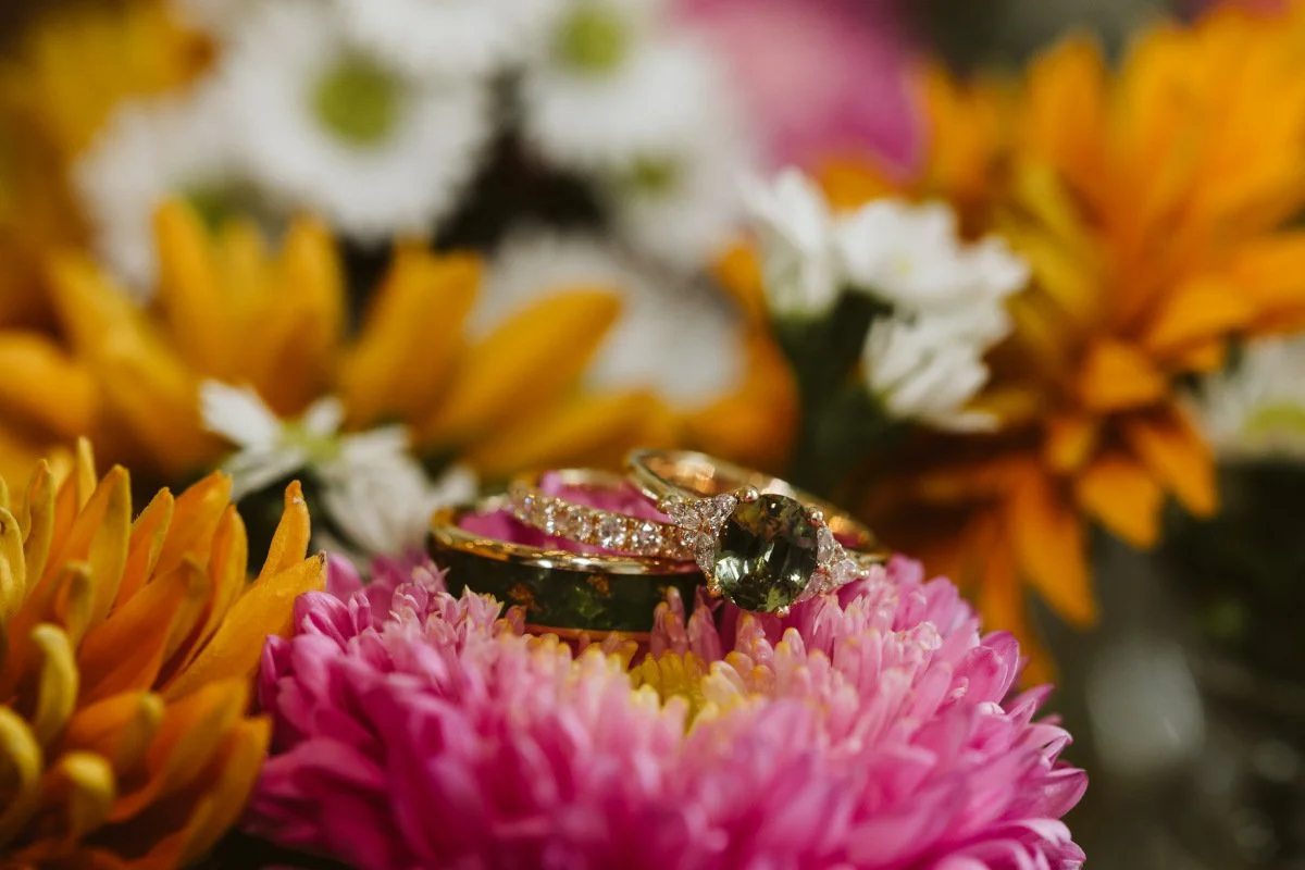 Gold rings with gemstones resting on pink and orange flowers placed under the altar at a wedding ceremony in St. Louis