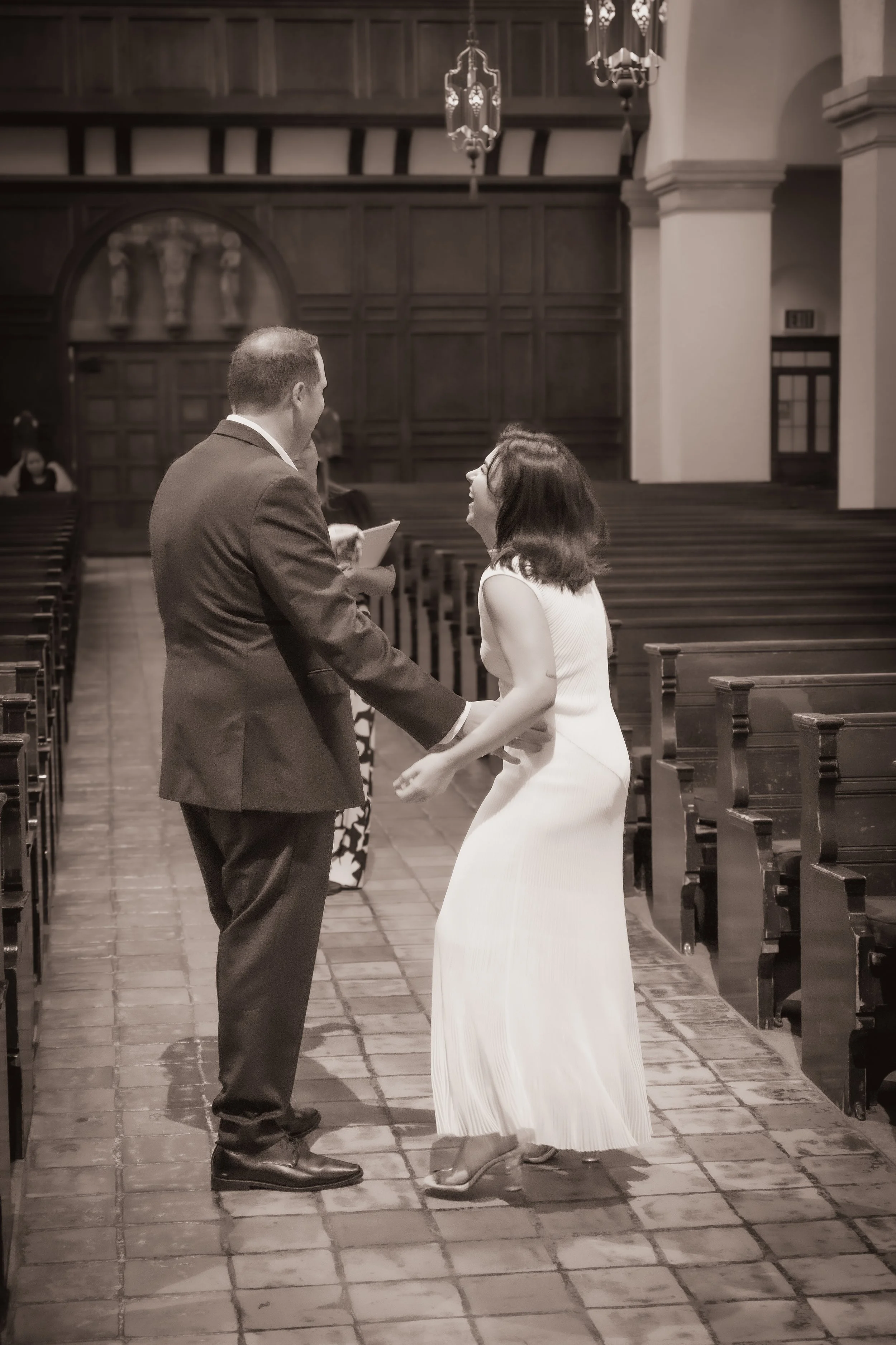 A woman and a man holding hands and smiling at each other inside a church during a wedding ceremony.