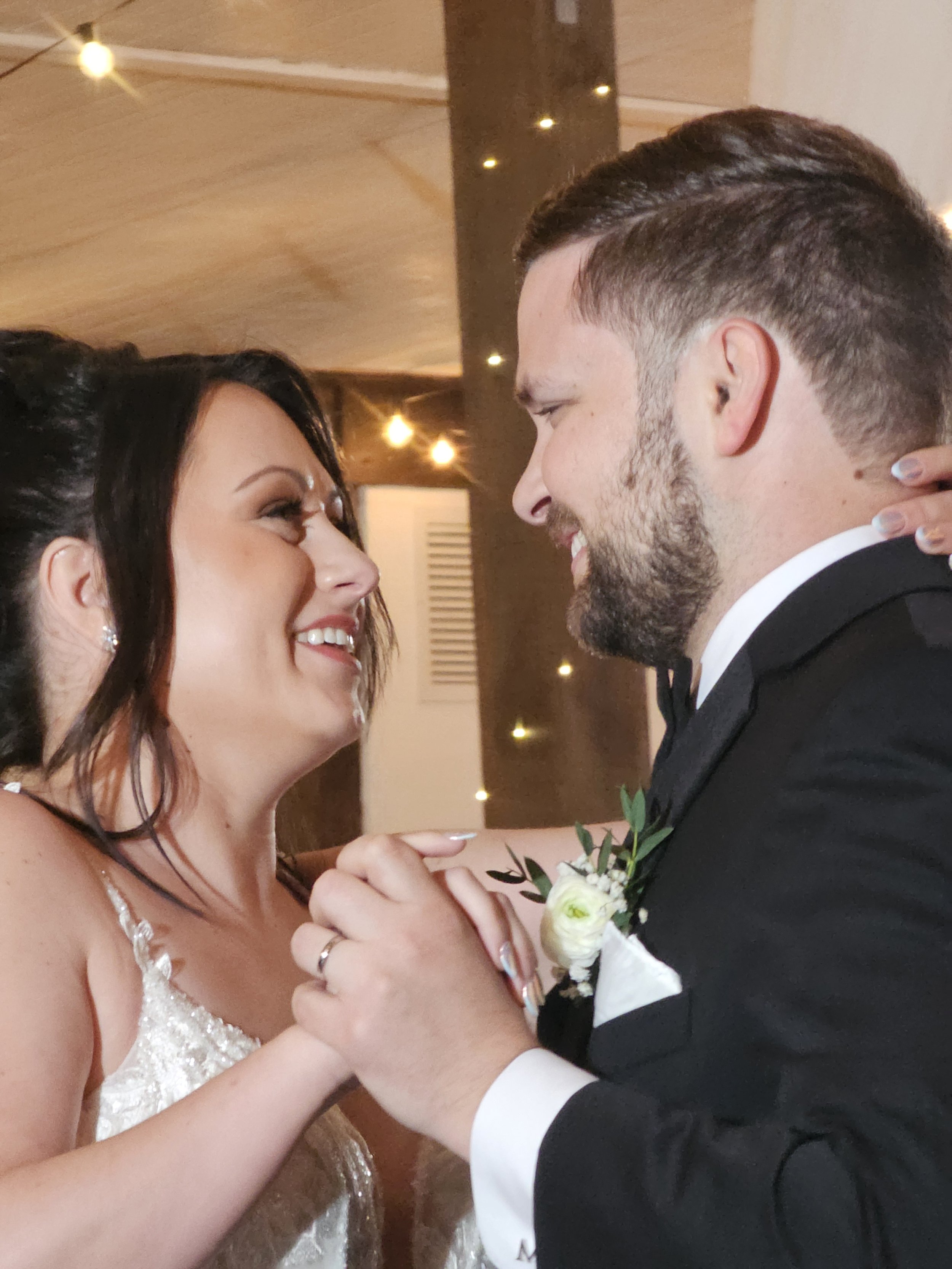 A bride and groom share a dance, smiling and looking into each other's eyes, holding hands at their wedding reception.