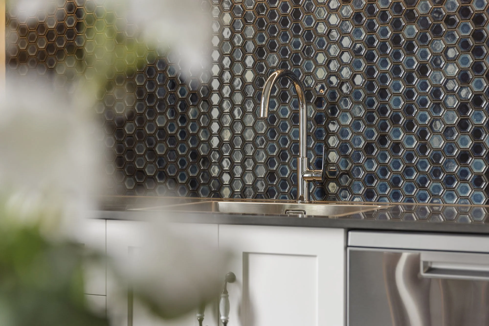Modern kitchen with a stainless steel faucet, dark hexagonal tile backsplash, white cabinets, and a stainless steel appliance.