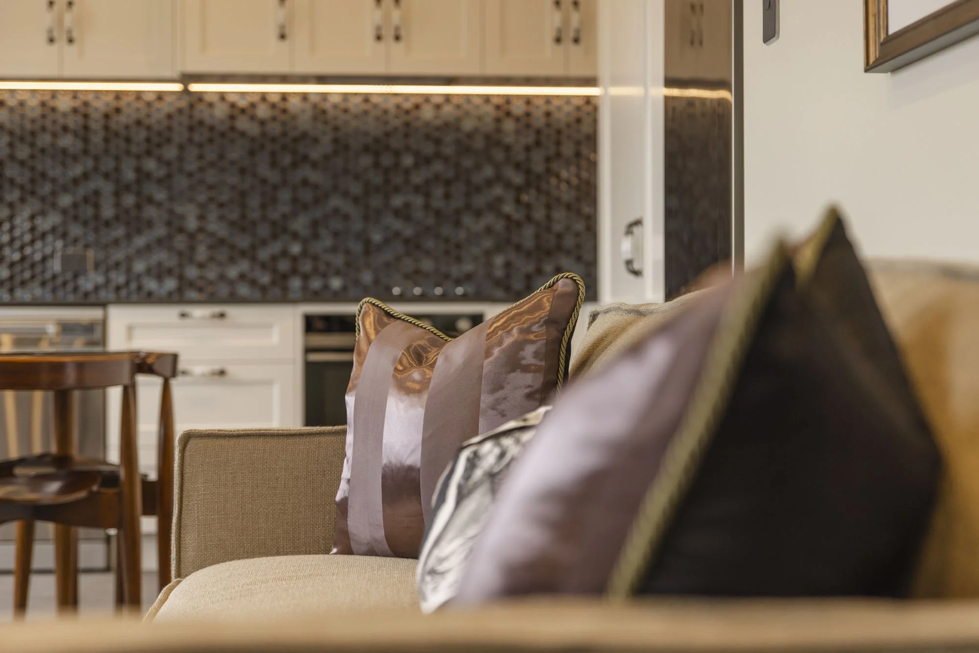 Close-up of decorative throw pillows on a sofa in a modern living room with kitchen in the background.