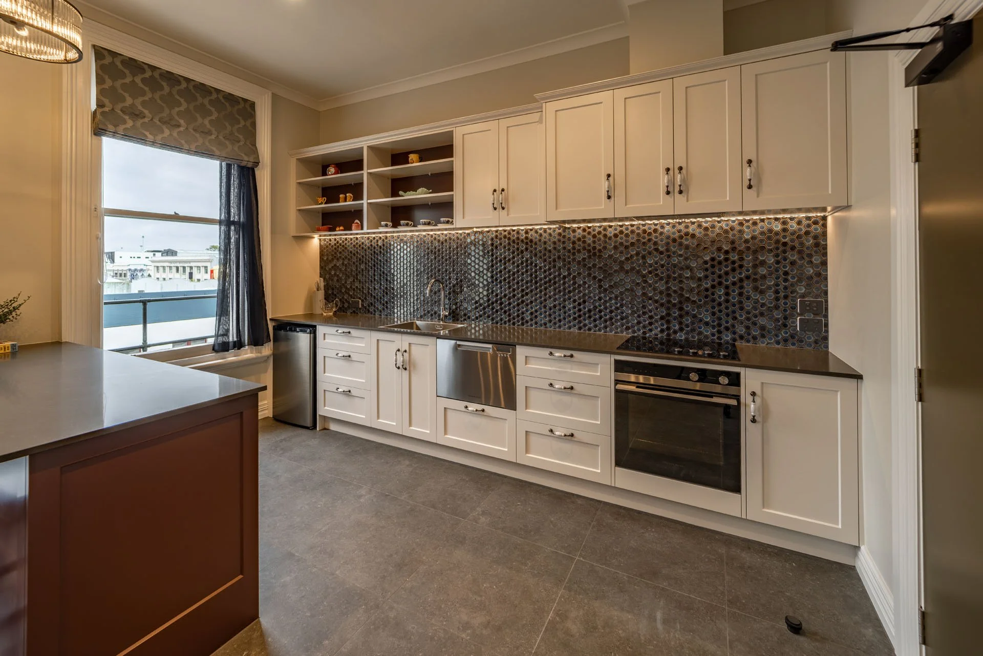 Modern kitchen with white cabinetry, patterned backsplash, stainless steel appliances, and a window with curtain.