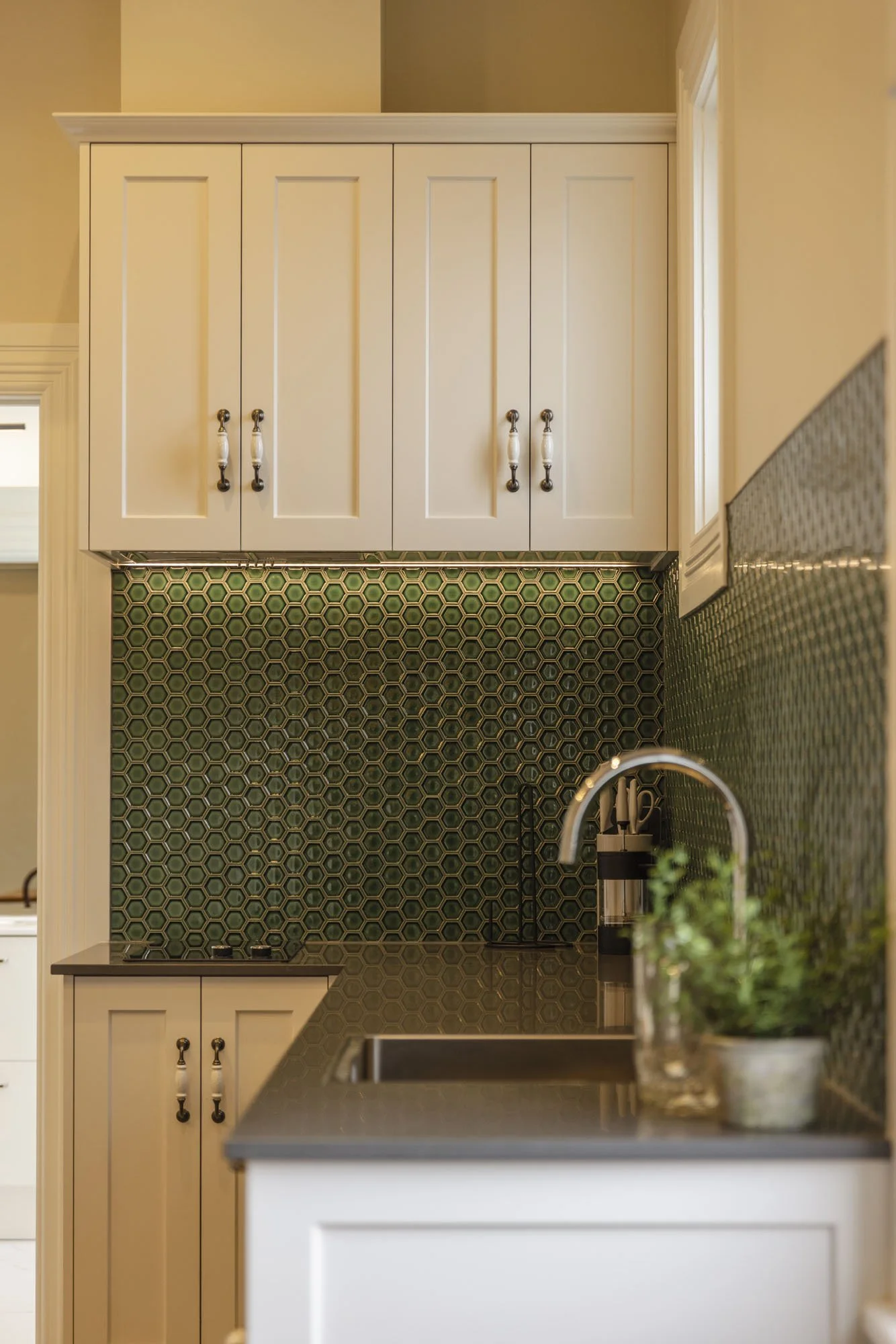 View of a kitchen corner with white cabinets, green hexagonal tile backsplash, and a black countertop with a sink.