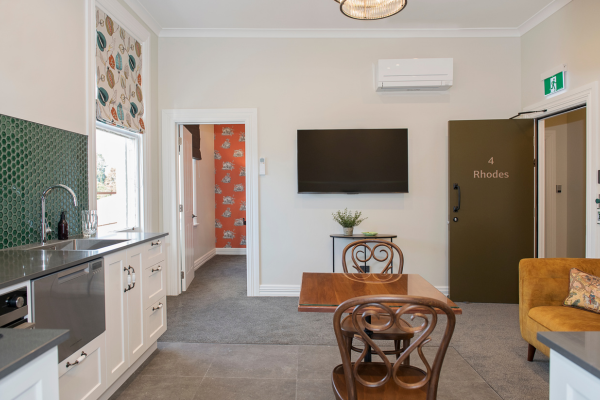 Interior of a living room and kitchen area with a TV, dining table, chairs, and a mustard-colored sofa.