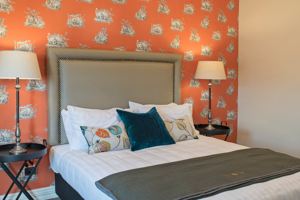 Bedroom with a large upholstered headboard, orange and white patterned wallpaper, and two matching bedside lamps.