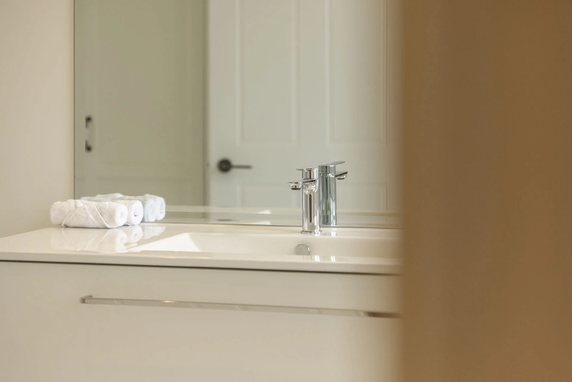 Bathroom vanity with folded white towels, mirror, and chrome faucet, with a door reflected in the mirror.