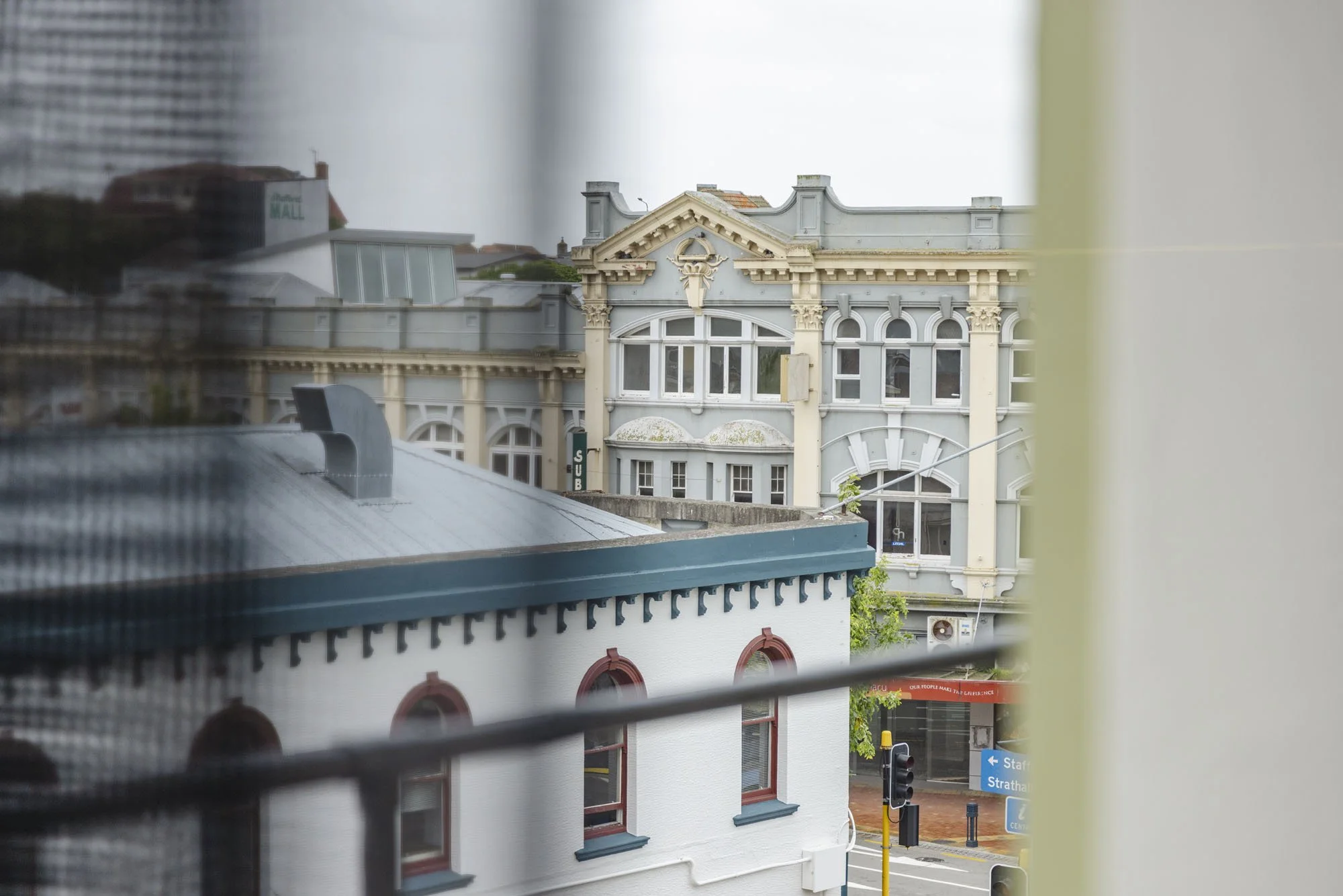 View of historic buildings through a window with a screen, showing detailed architecture with arched windows and decorative elements.
