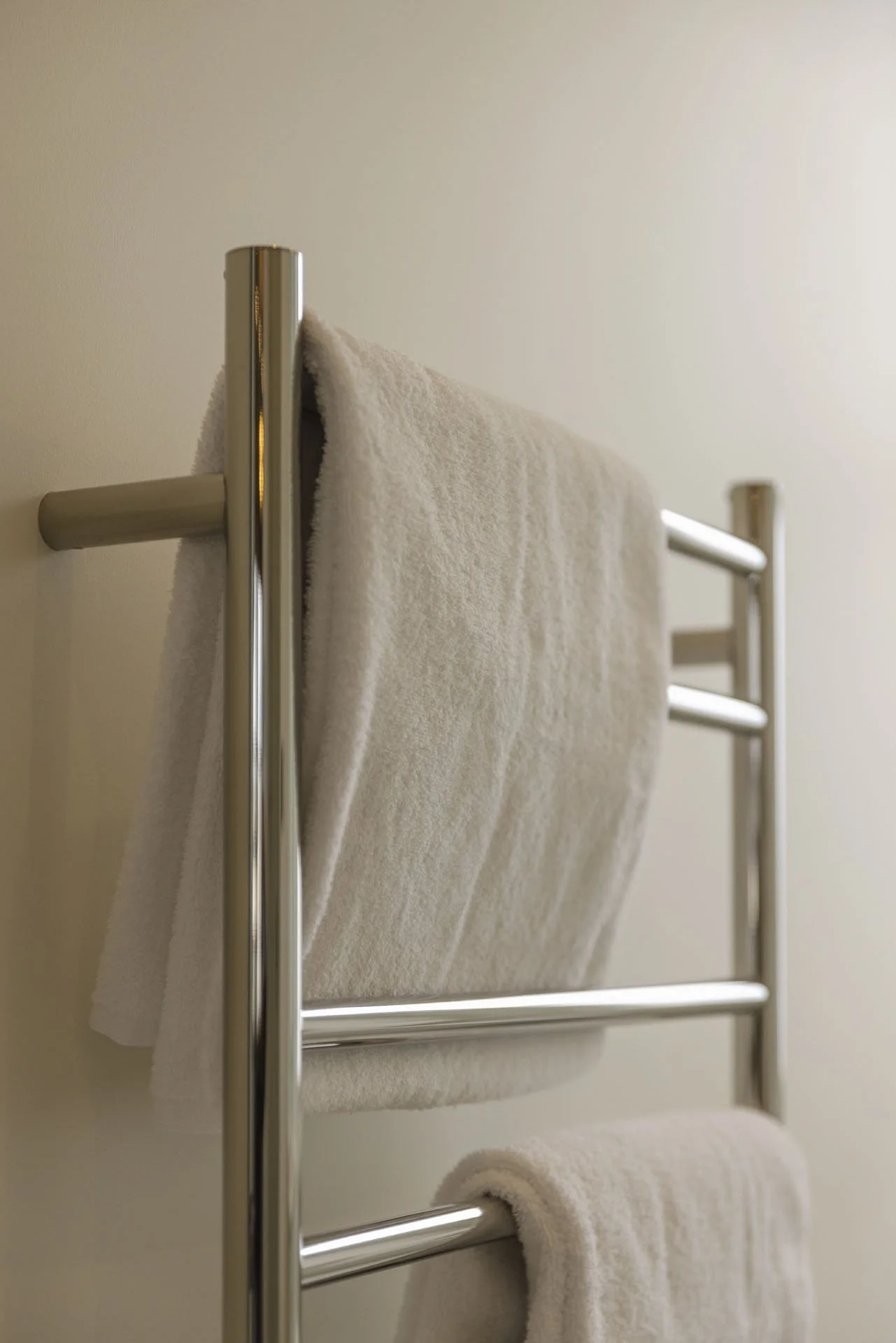 A close-up of a wall-mounted chrome towel rack with two white towels hanging on it.