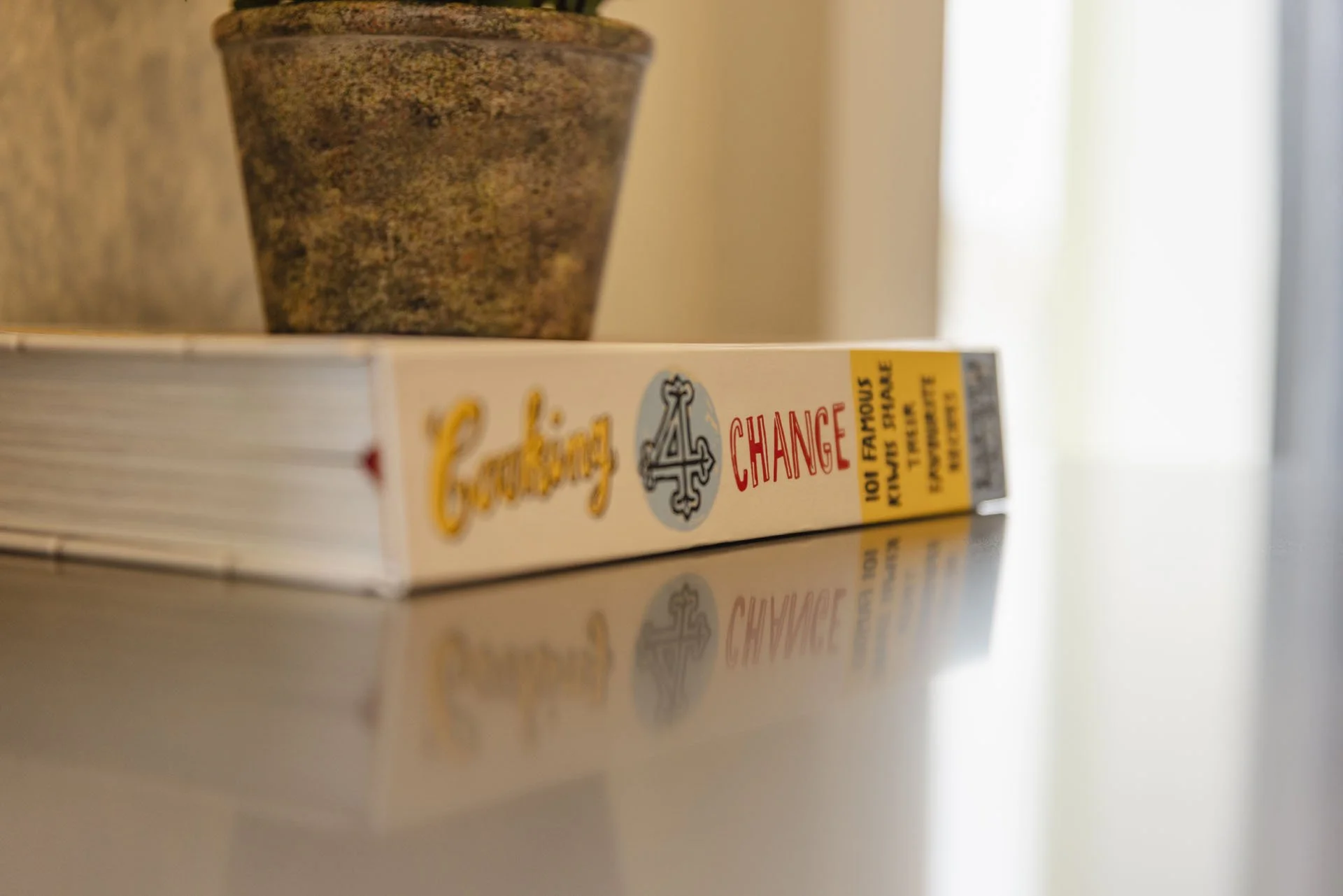 A deck of Monopoly Change cards with a gray stone bowl on top, placed on a reflective surface near a window.