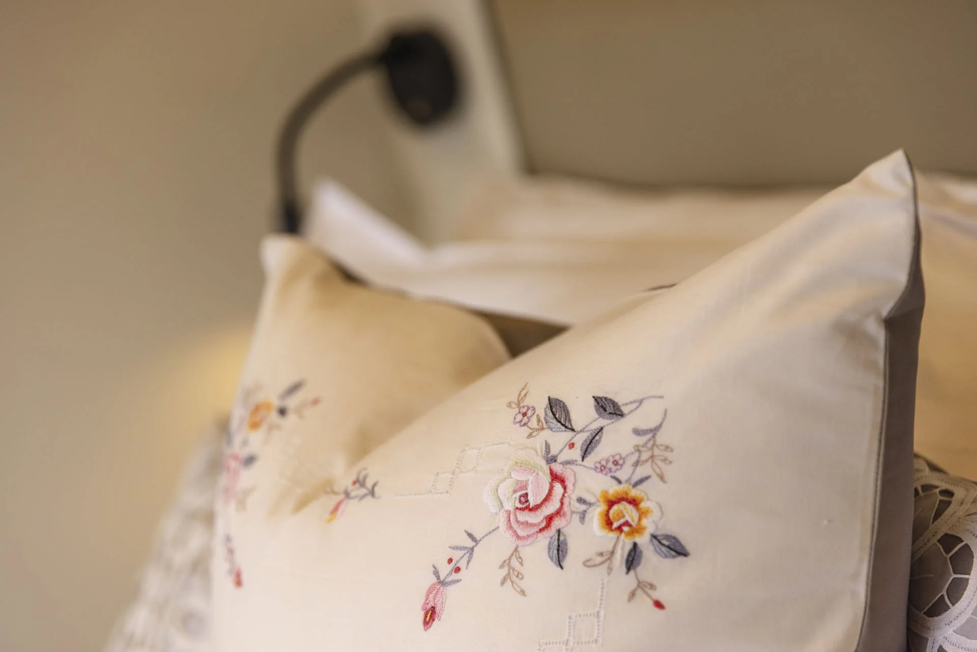 Close-up of embroidered decorative pillows on a bed, featuring floral designs in pastel colors.
