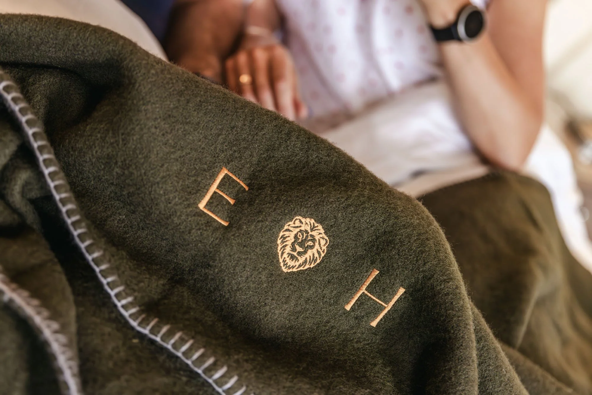 Close-up of a dark green fleece jacket with the word "EOHI" and a lion's face embroidered in orange, with a person in a white shirt in the background.