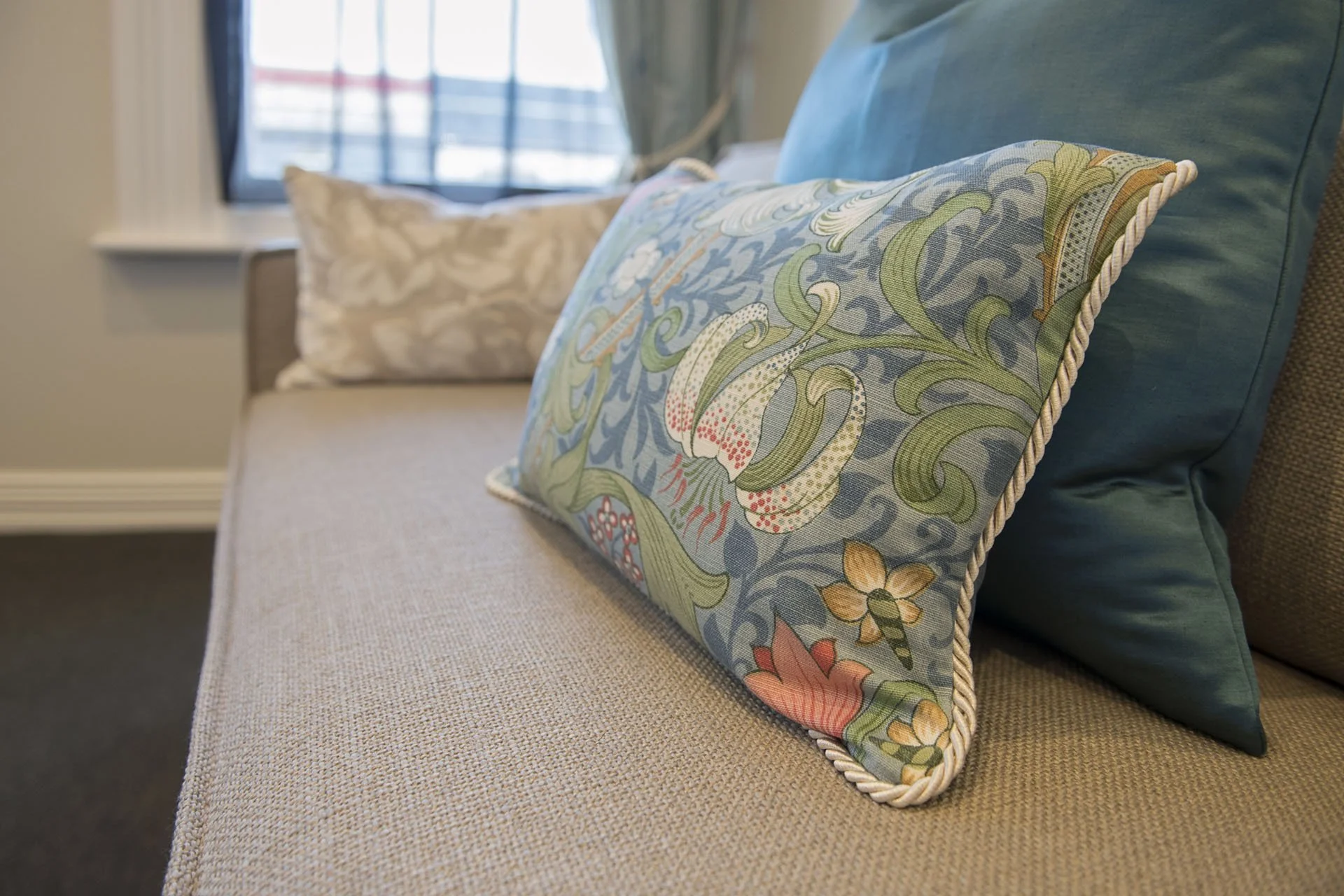 Decorative embroidered pillow with floral patterns on a beige couch in a room with a window.